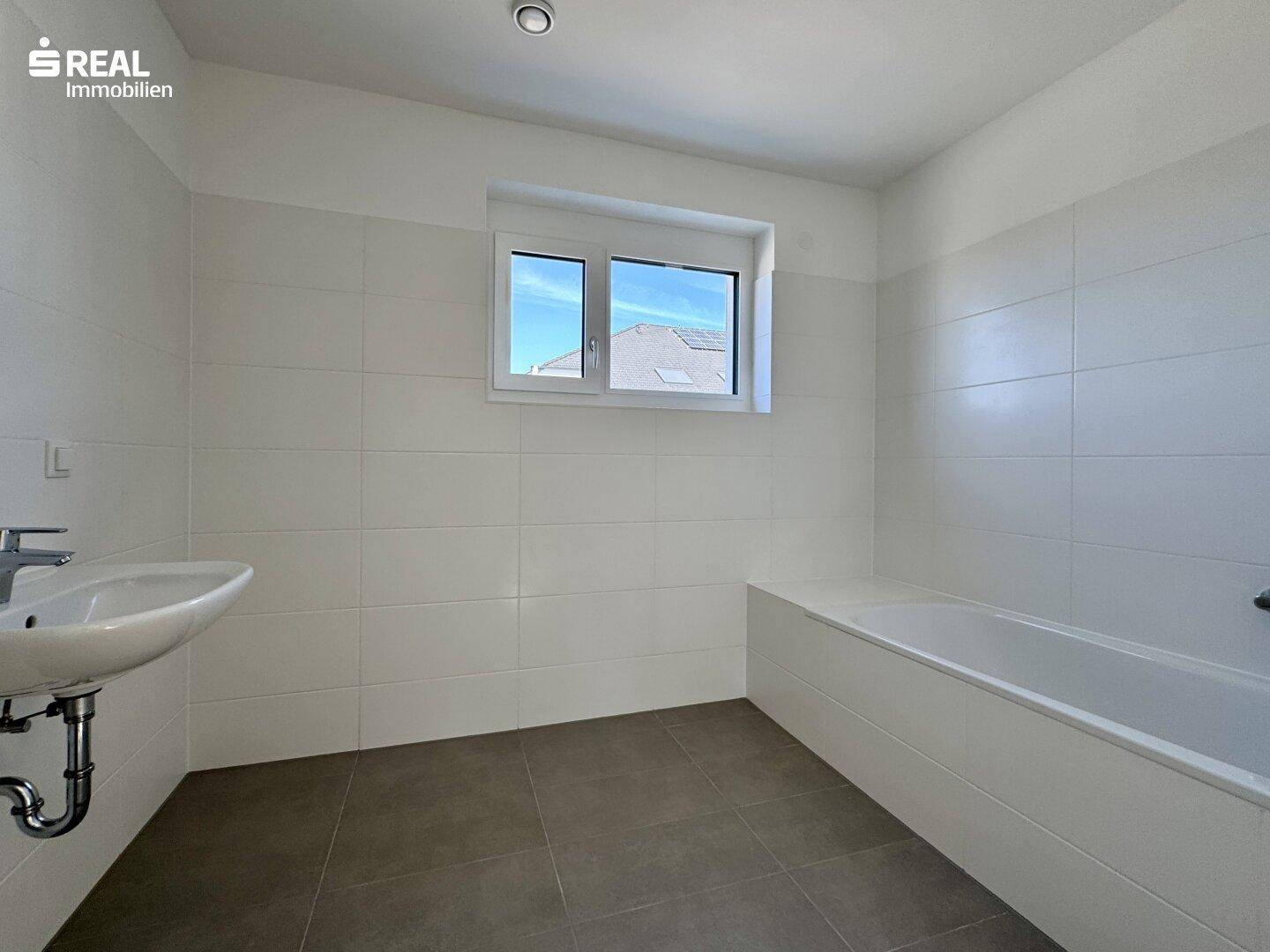 Modernes Badezimmer mit weißen Fliesen, Badewanne und Waschbecken.