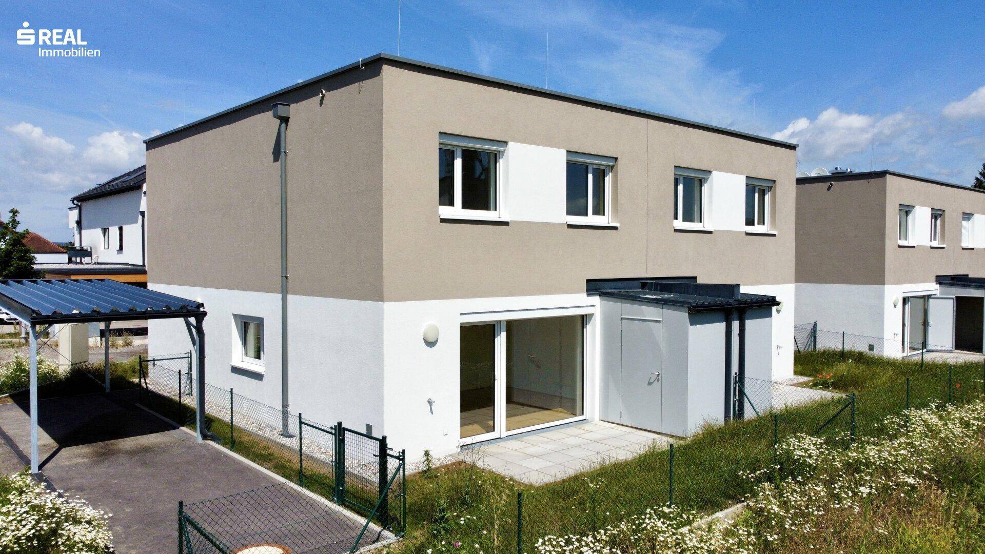 Rückseite eines modernen Reihenhauses mit Terrasse, Schuppen und Zugang zum Gartenbereich.