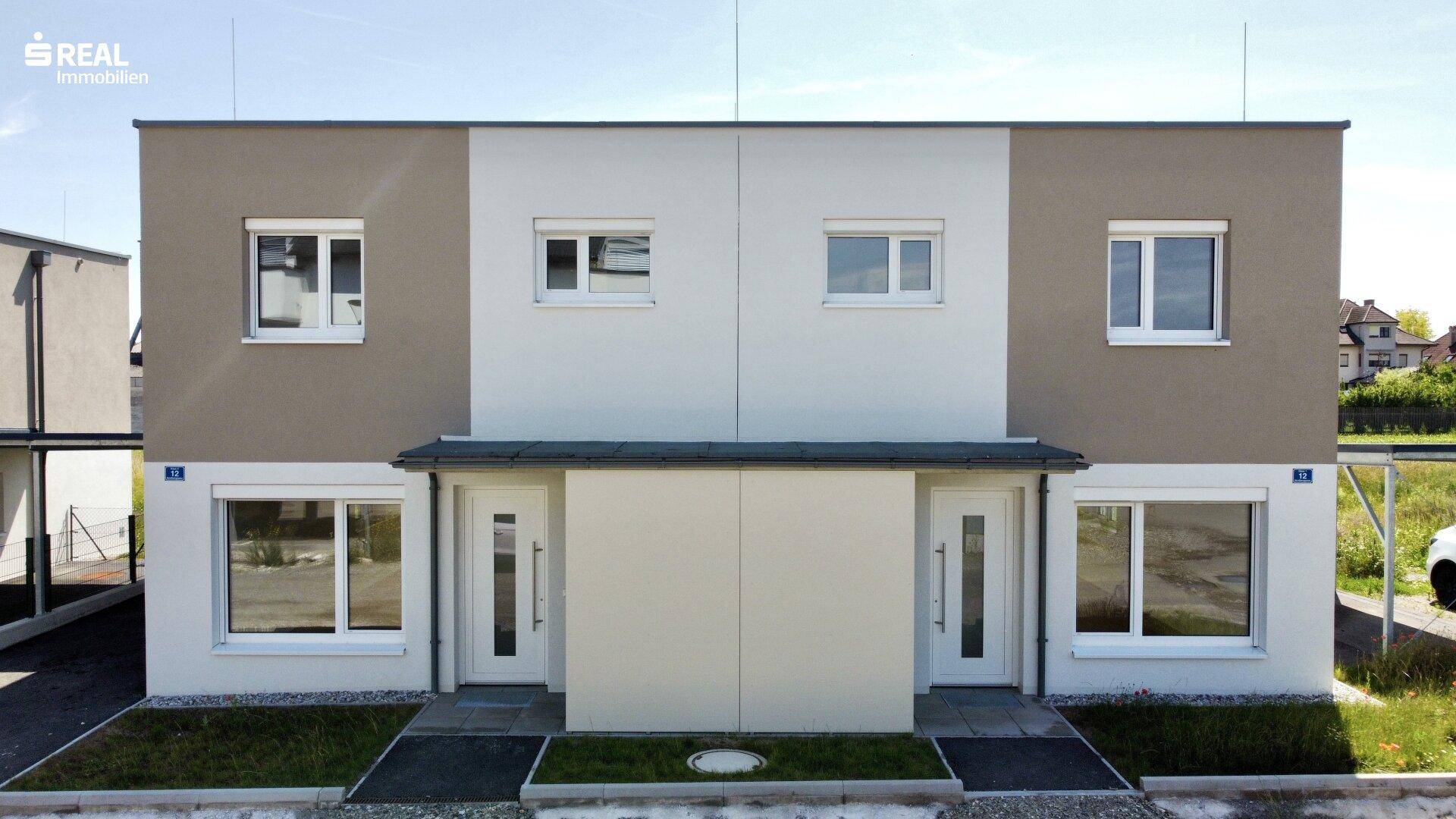 Vorderansicht von zwei modernen Reihenhäusern mit zweifarbiger Fassade und Eingangsbereichen.