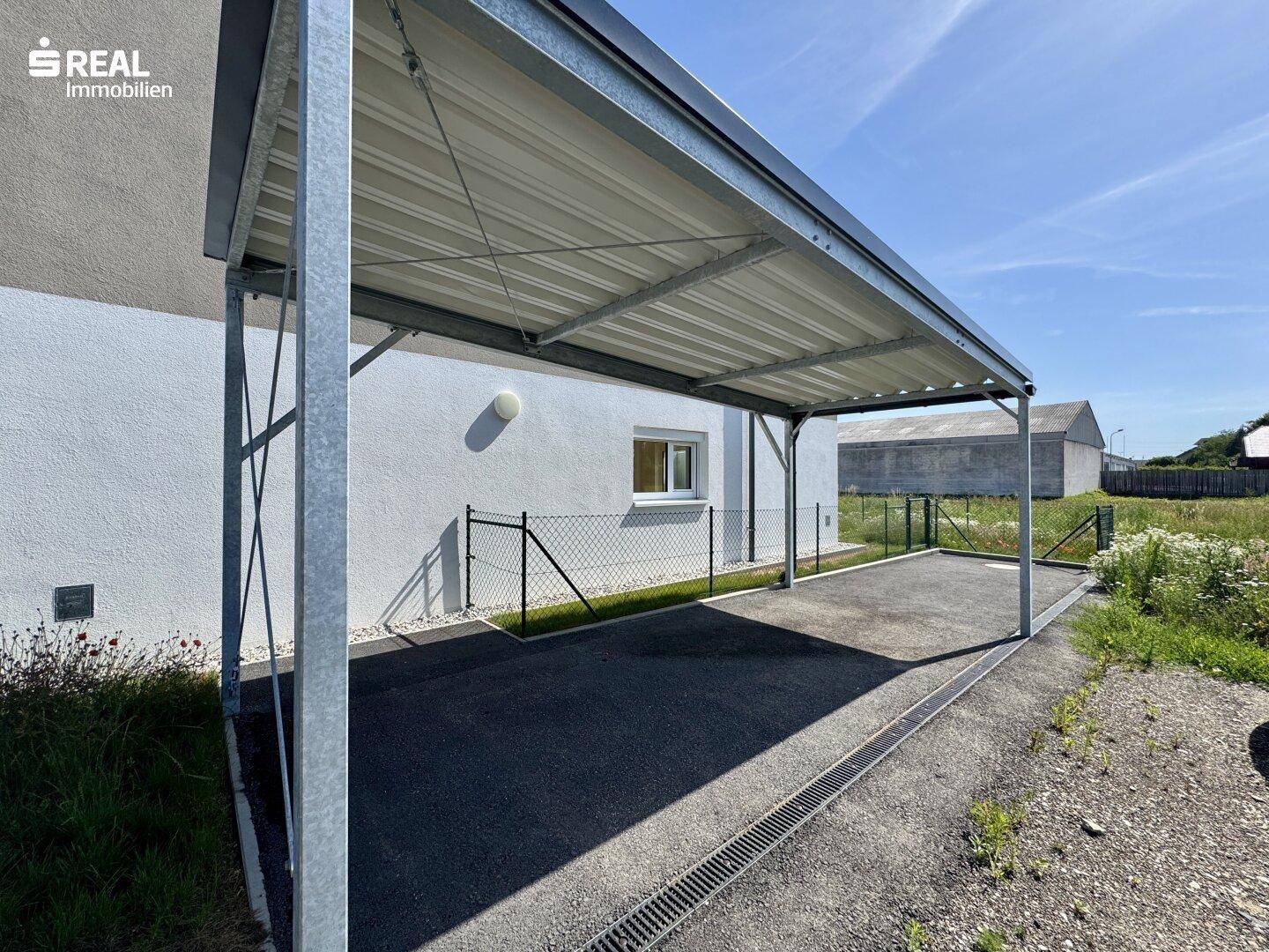 Überdachter Carport-Bereich neben einem Reihenhaus, bietet Schutz für Fahrzeuge.