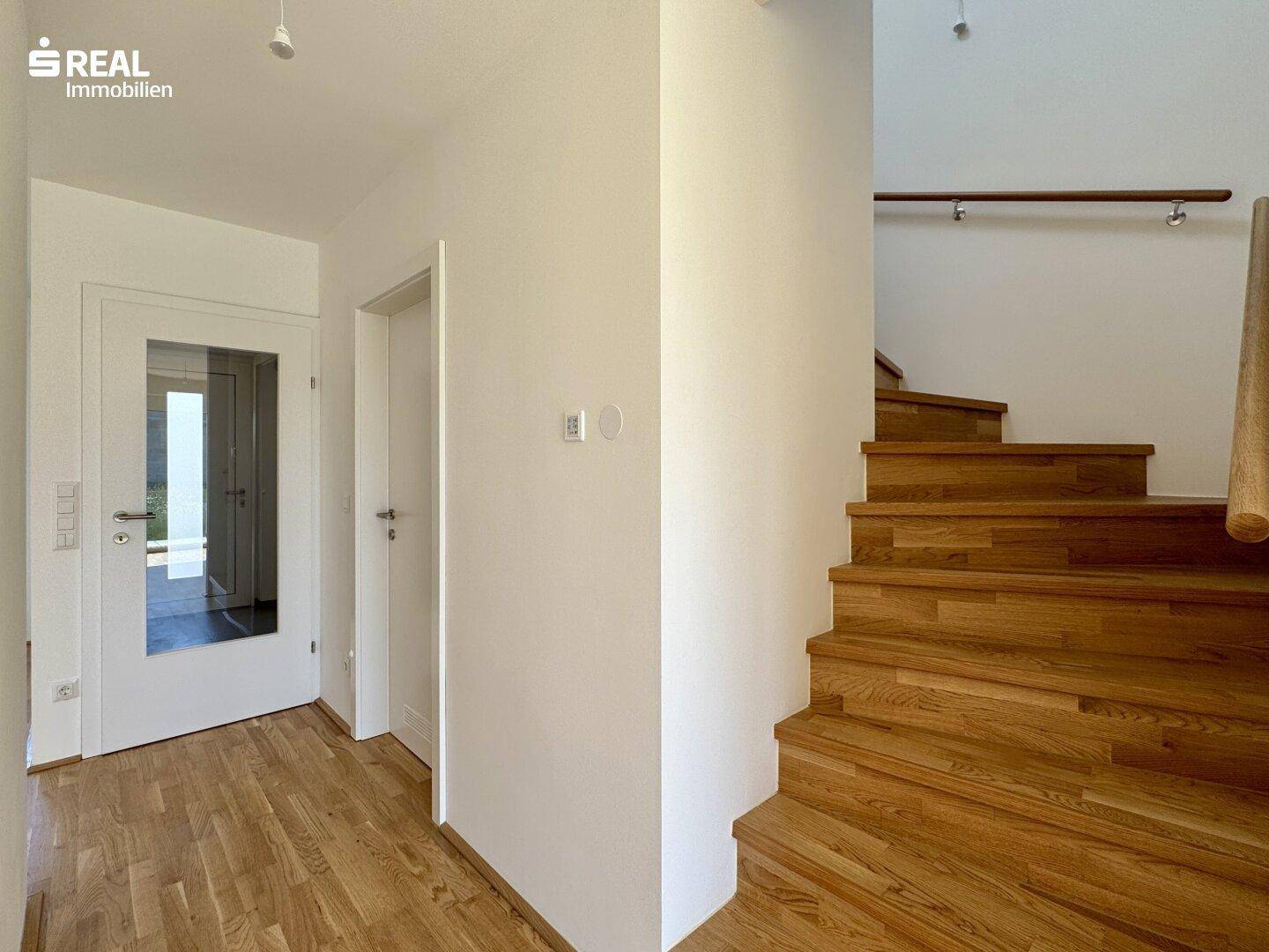 Heller Flur mit Holztreppe zum Obergeschoss und Parkettboden.