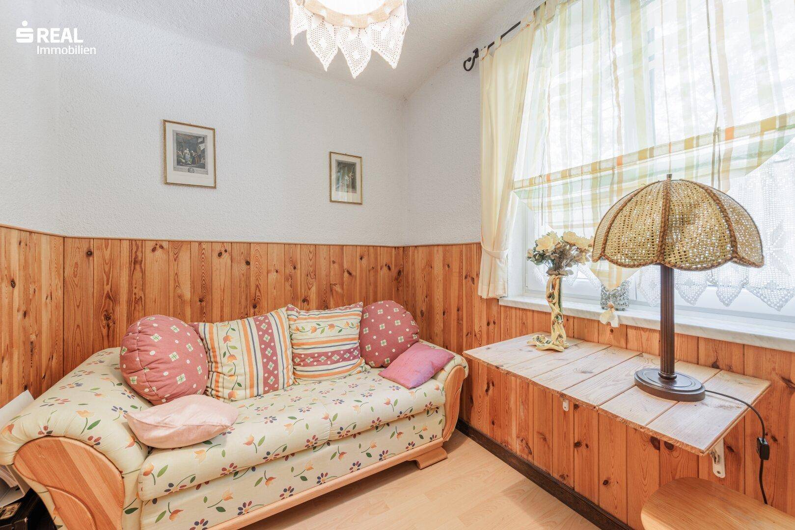 Kleines Schlafzimmer mit Holzvertäfelung, Tagesbett und einem Fenster für natürliches Licht.