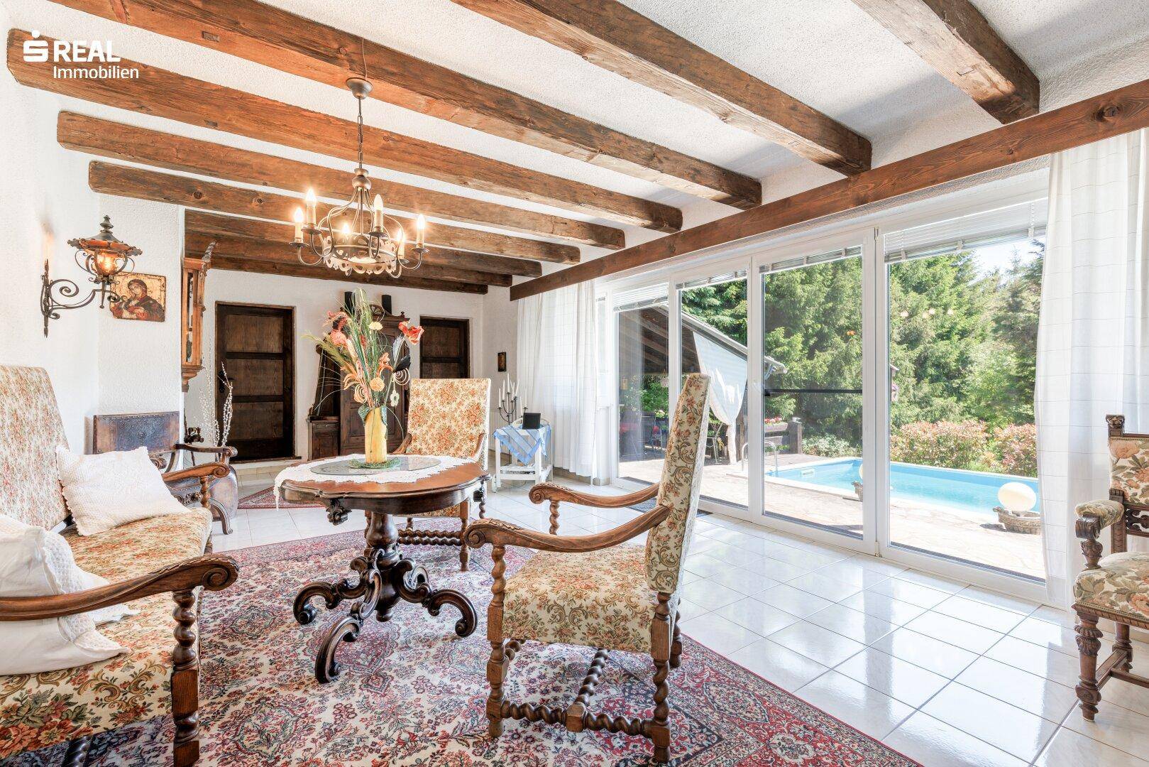 Gemütliches Wohnzimmer mit Holzbalkendecke, traditionellen Möbeln und Blick auf den Pool.