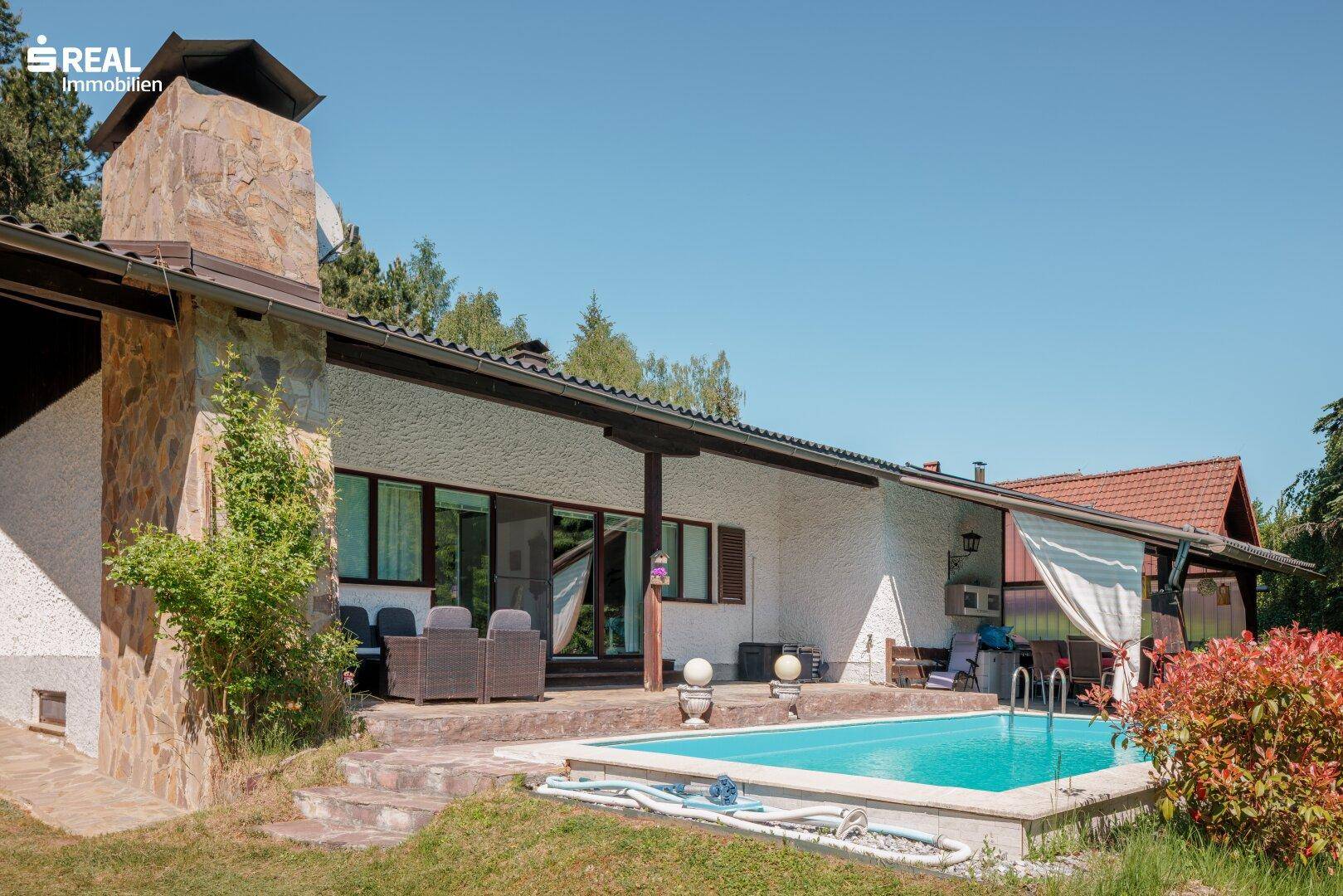 Seitenansicht des Hauses mit Poolbereich, Steinfassade und überdachter Terrasse.