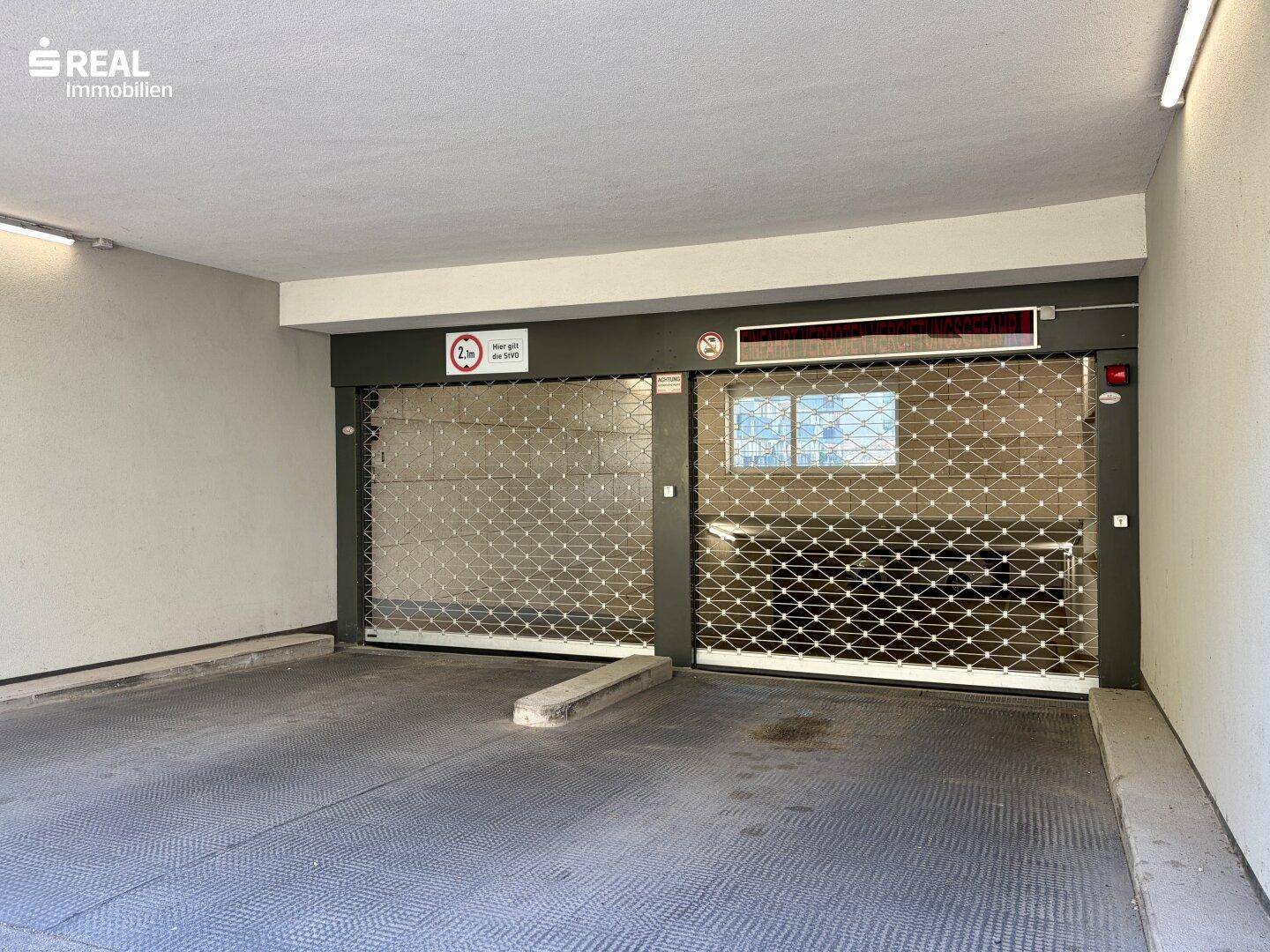 Nahaufnahme des Tiefgarageneingangs mit geschlossenen Rolltoren und Höhenbegrenzung.