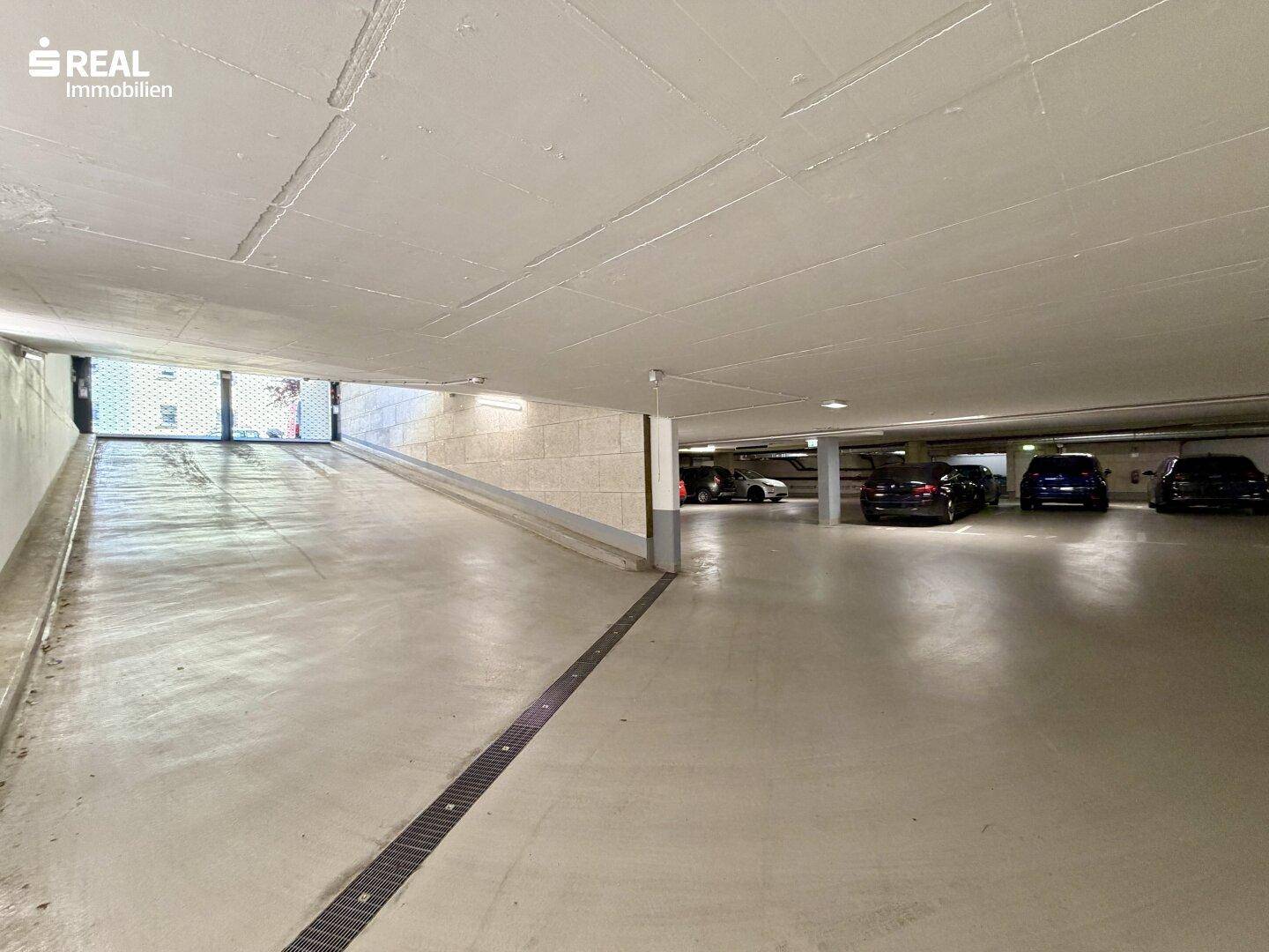 Helle Rampe führt in die geräumige Tiefgarage mit markierten Stellplätzen.