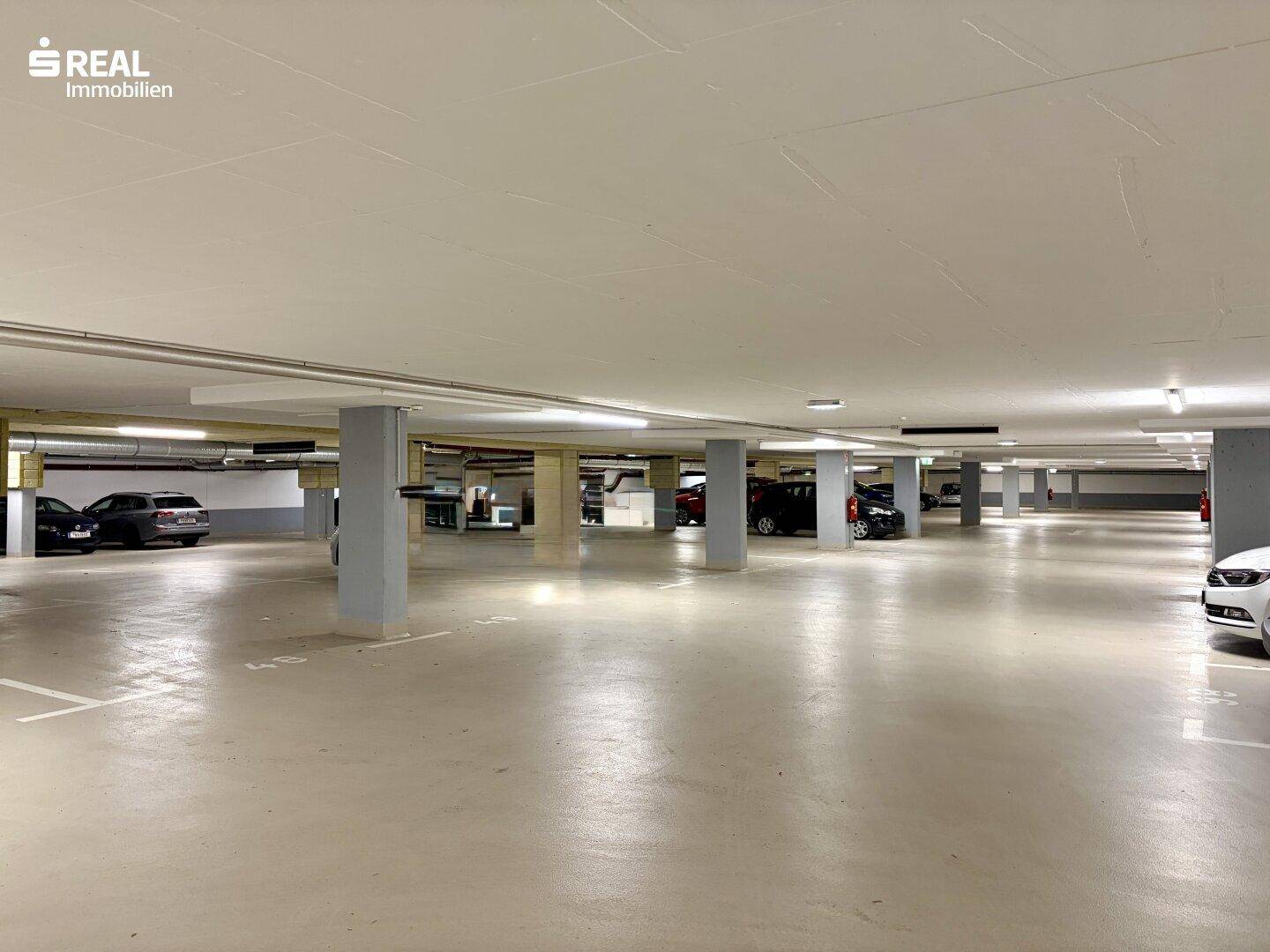 Weitläufige Tiefgarage mit vielen markierten Stellplätzen und guter Beleuchtung.