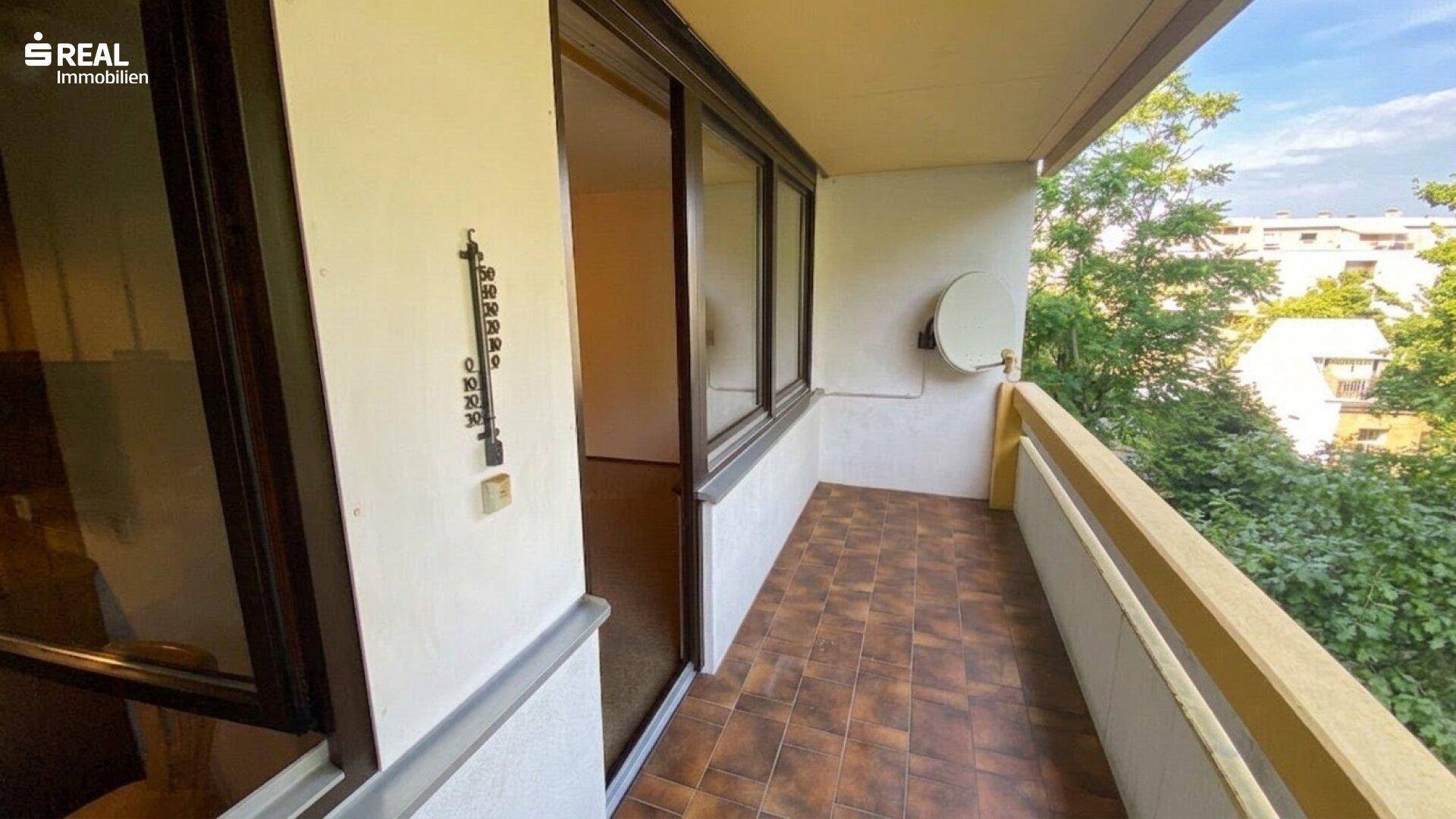 Schmaler Balkon mit braunen Fliesen, Satellitenschüssel und Blick auf die Umgebung.