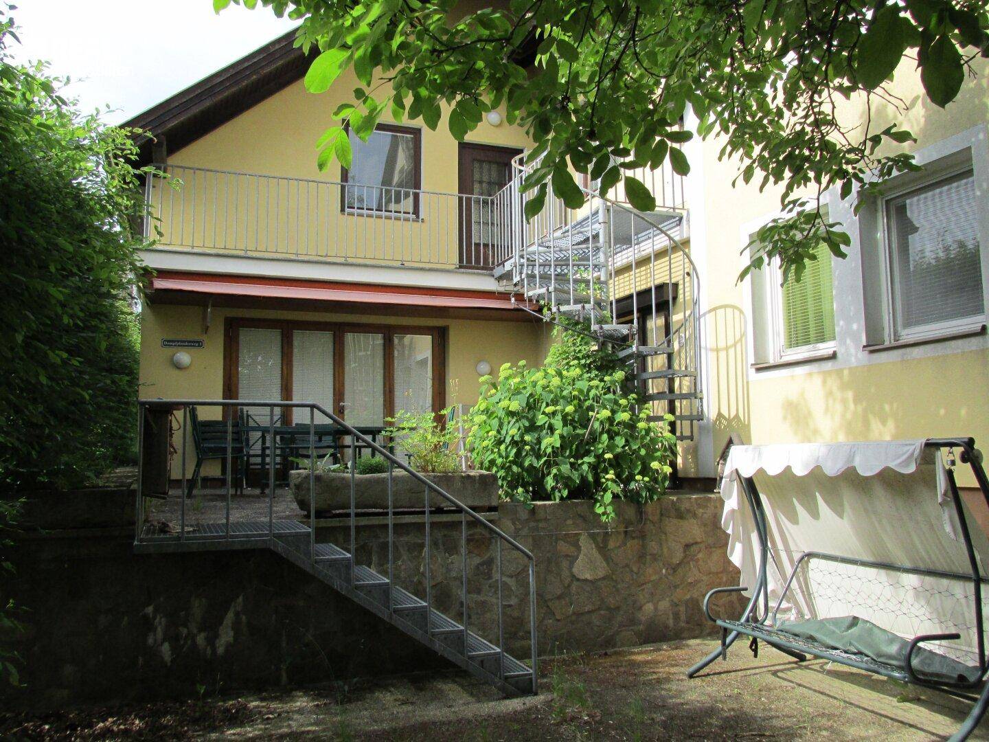Gemütliche Terrasse mit Sitzgelegenheiten und Zugang zu einem Balkon über eine Wendeltreppe.