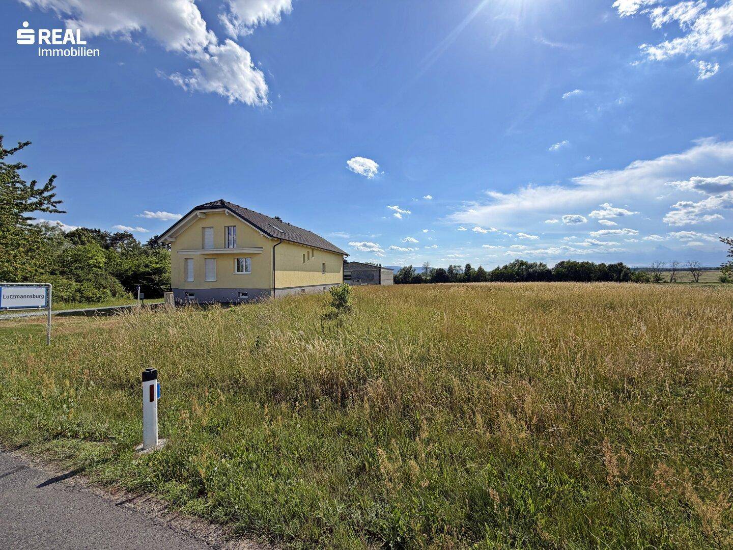 Gelbes Wohnhaus mit weitem Feld im Vordergrund und sonnigem Himmel.