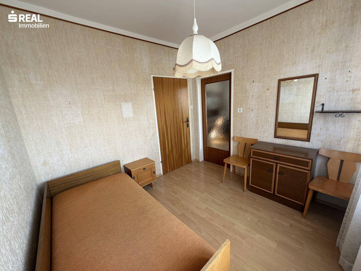 Kleines Schlafzimmer mit Einzelbett, Nachttisch, Kommode und Laminatboden, ideal als Gästezimmer.