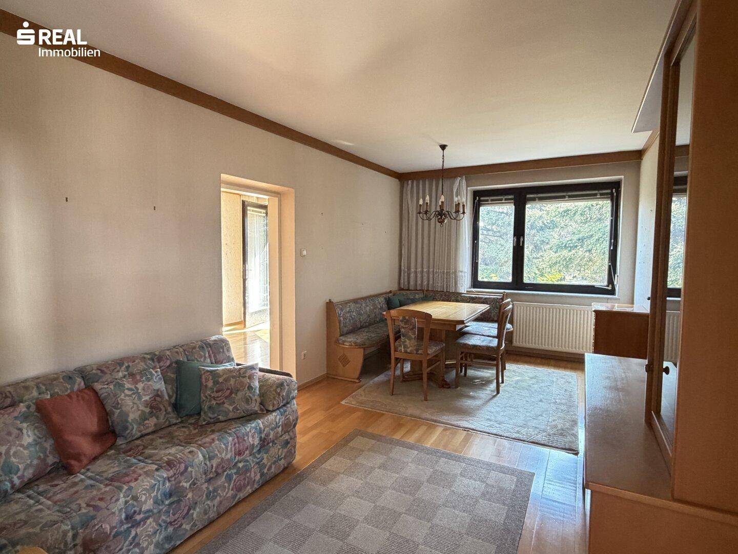 Kombinierter Wohn- und Essbereich mit Sofa, Eckbank und Blick ins Grüne durch die Fenster.