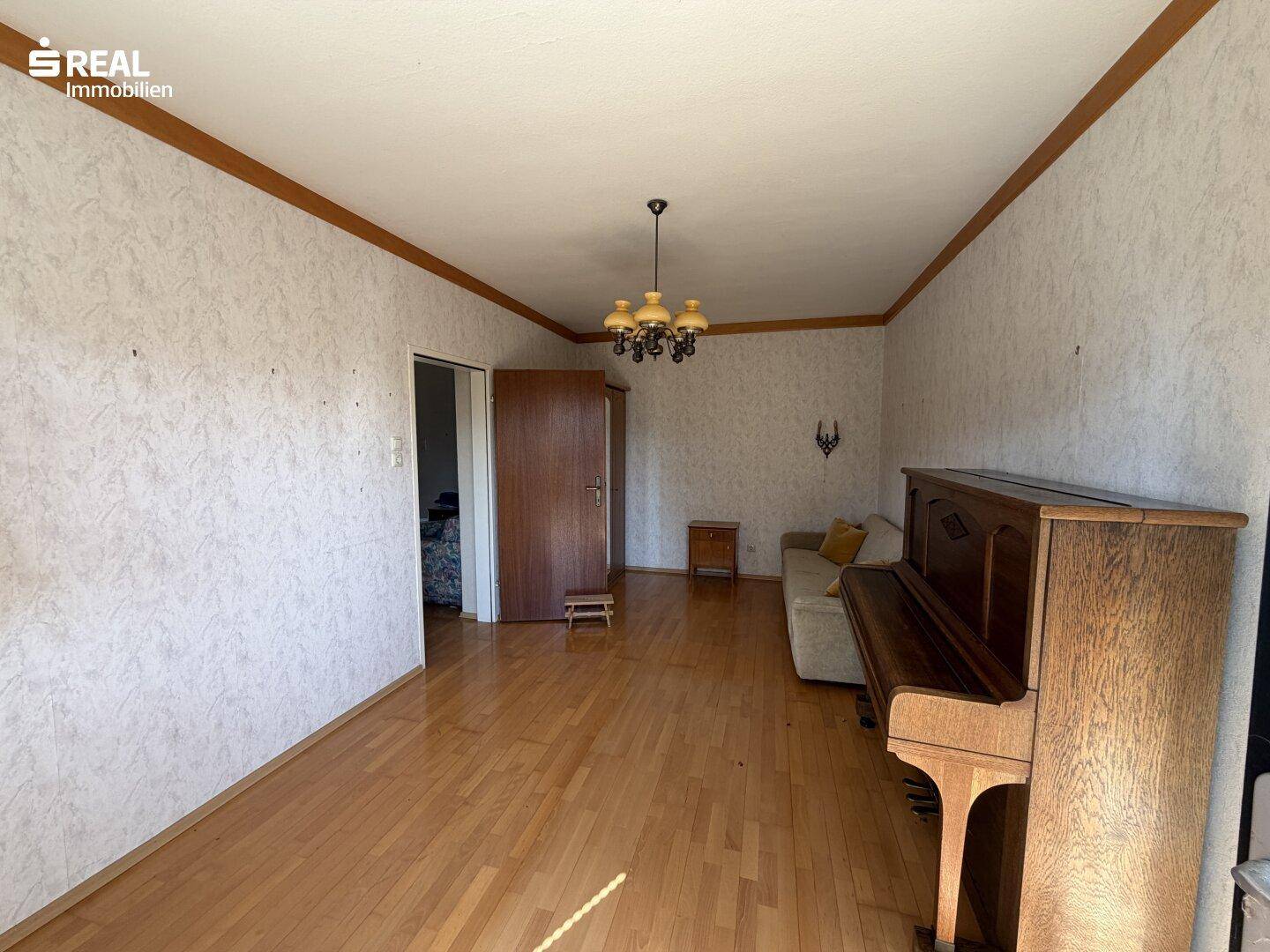 Helles Wohnzimmer mit Klavier, Sofa und Parkettboden, das eine einladende Atmosphäre schafft.