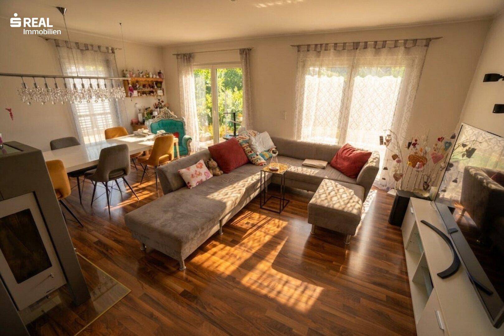 Heller Wohn- und Essbereich mit Holzboden, großem Sofa und Zugang zur Terrasse.