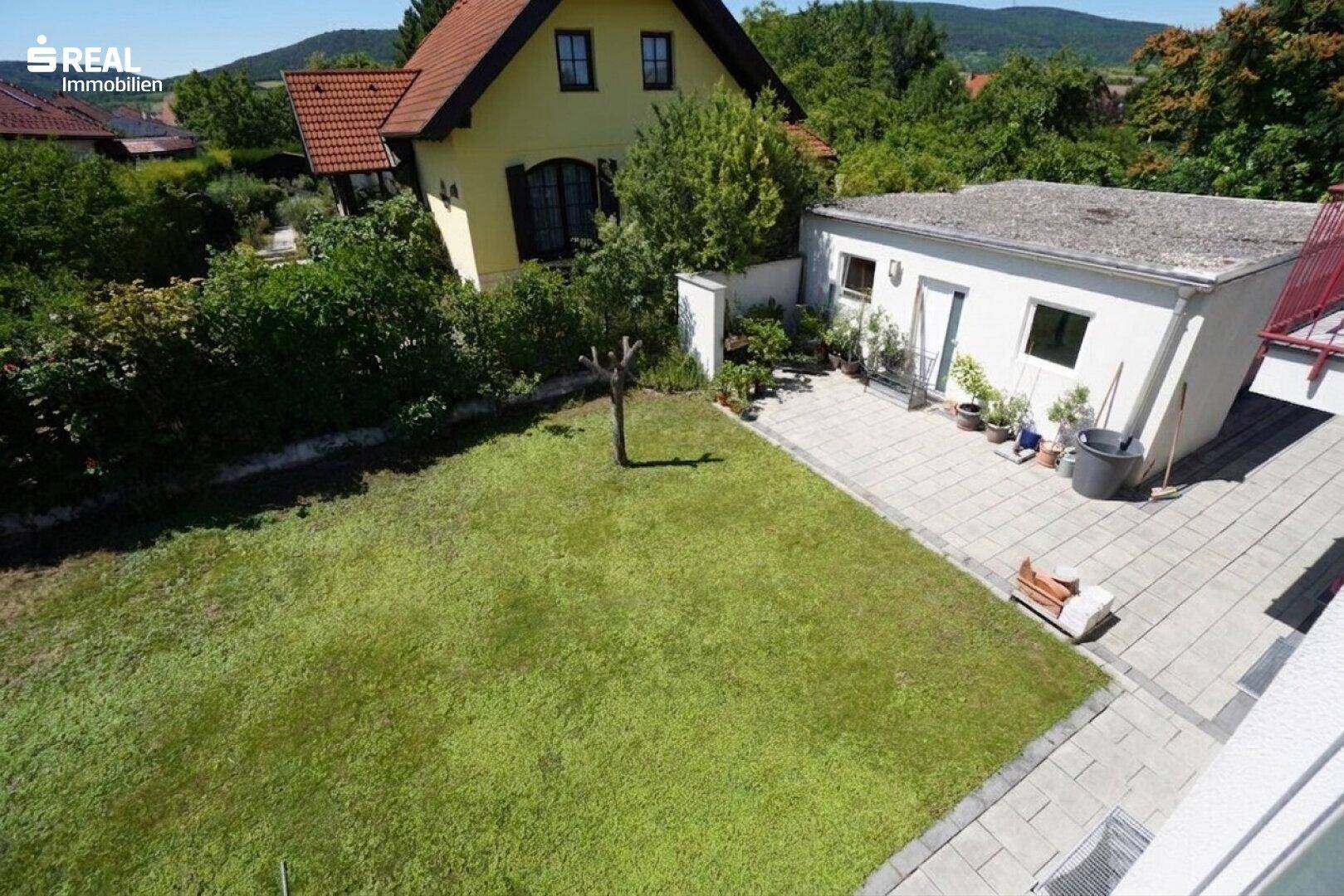Blick von oben auf den gepflegten Garten mit Rasenfläche und gepflastertem Bereich.