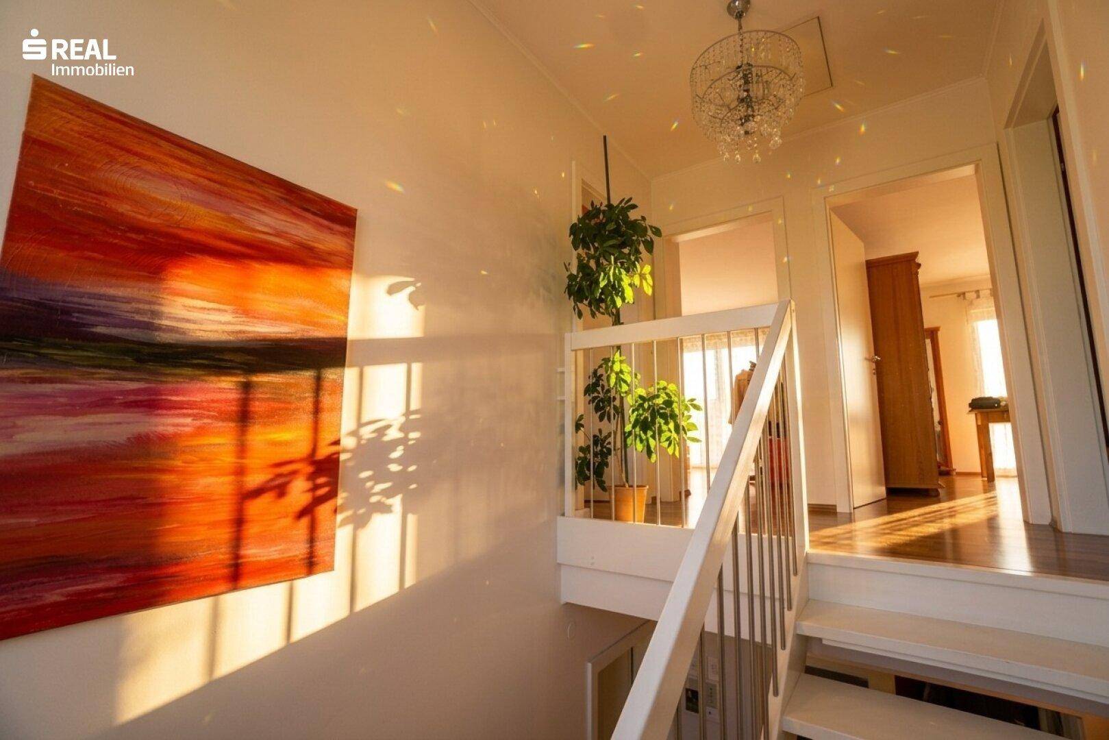 Lichtdurchfluteter Treppenaufgang mit Kunstwerk an der Wand und Pflanzen.