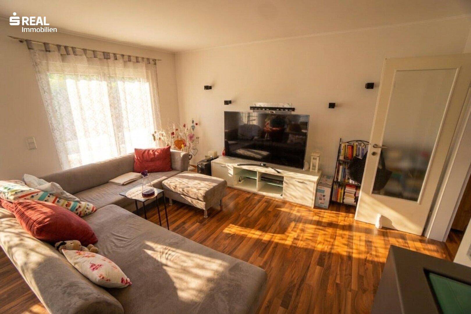 Gemütliches Wohnzimmer mit großem Ecksofa, Holzboden und viel natürlichem Licht.