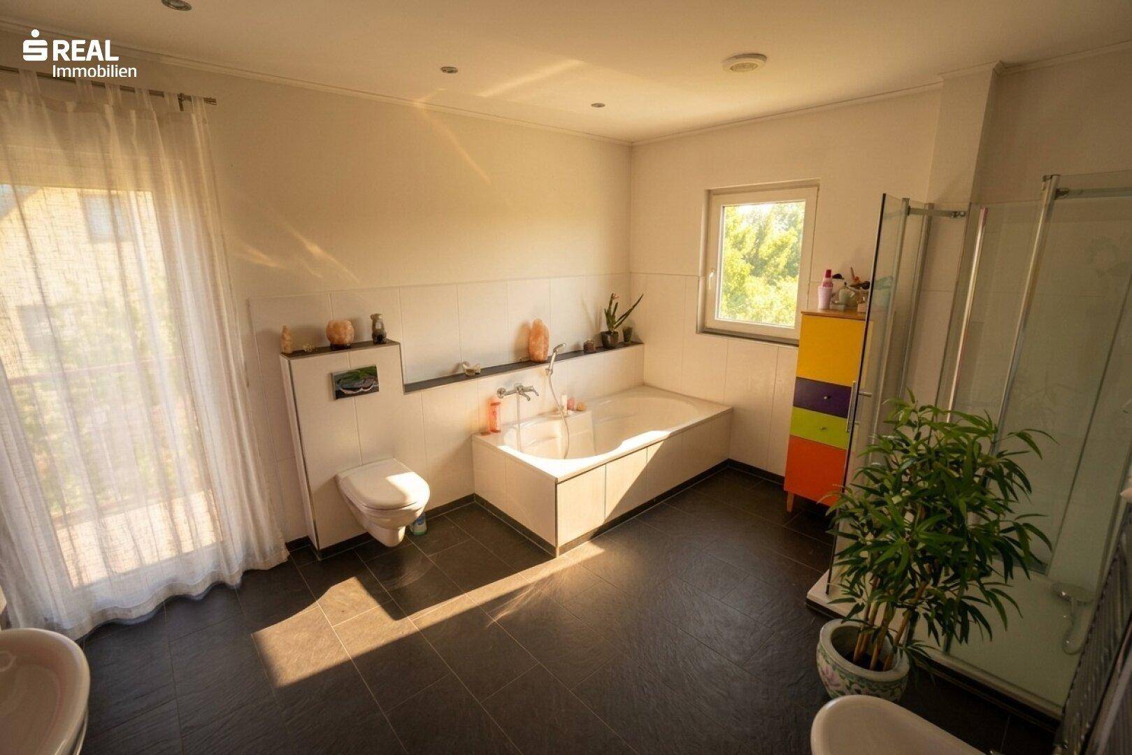 Geräumiges Badezimmer mit Badewanne, Dusche, WC und Fenster für Tageslicht.