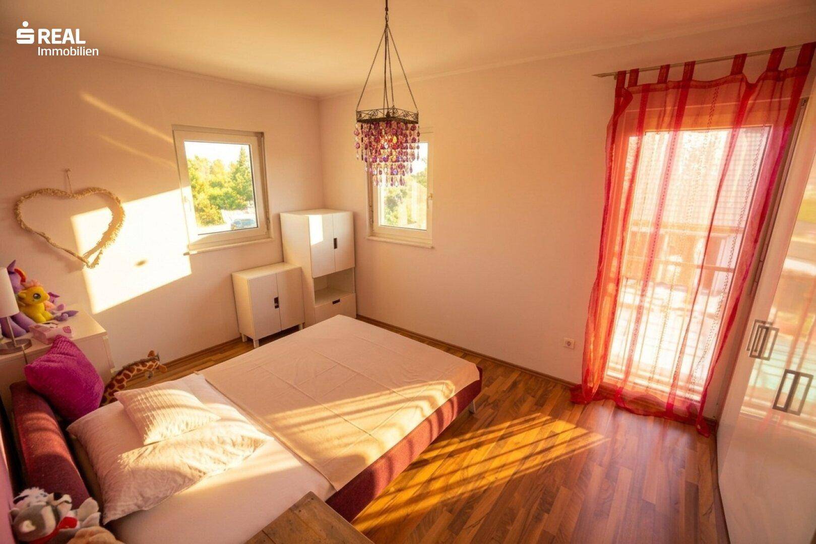 Helles Schlafzimmer mit Holzboden, Einzelbett und Fenster mit rotem Vorhang.