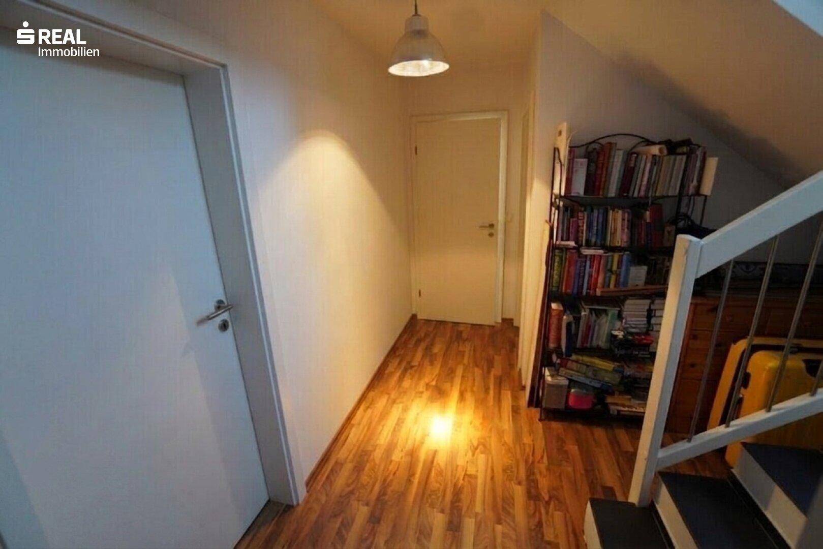 Heller Flur im Dachgeschoss mit Holzboden und Bücherregal.