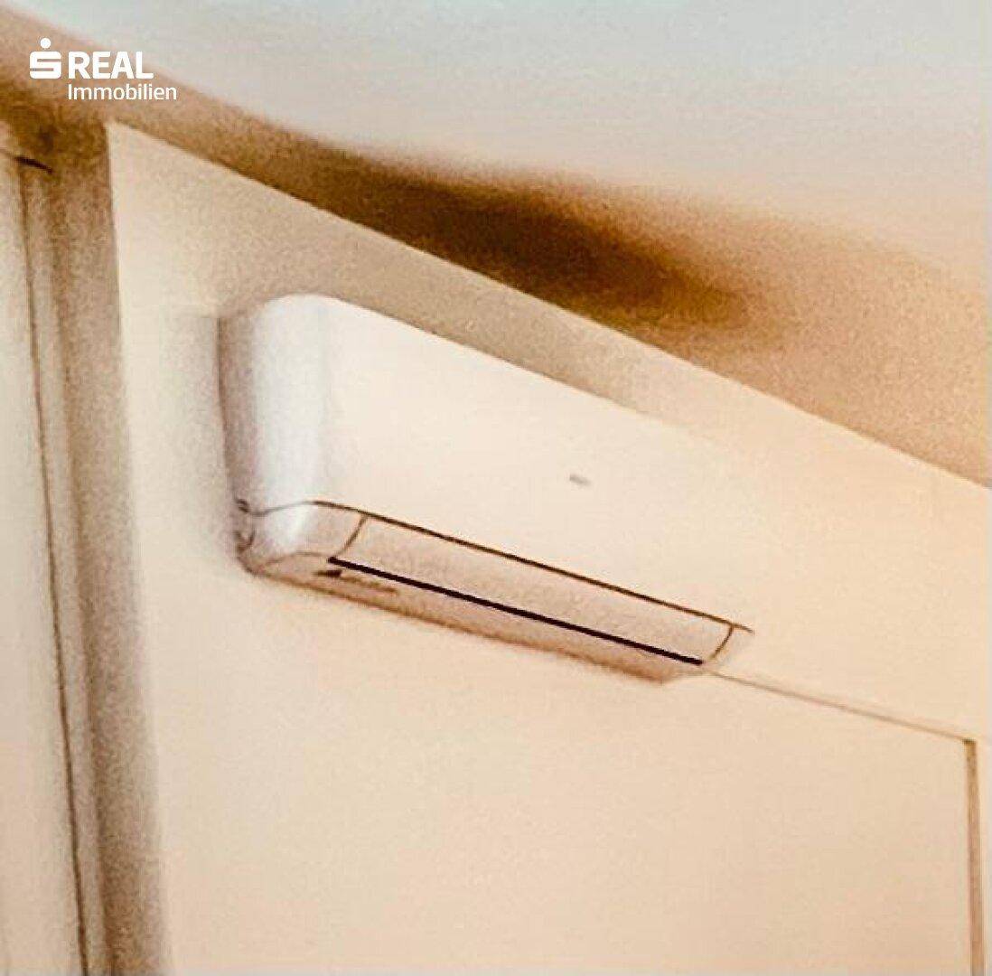Nahaufnahme einer Klimaanlage an einer weißen Wand, mit sichtbaren Verfärbungen darüber, die auf Wartungsbedarf hindeuten.