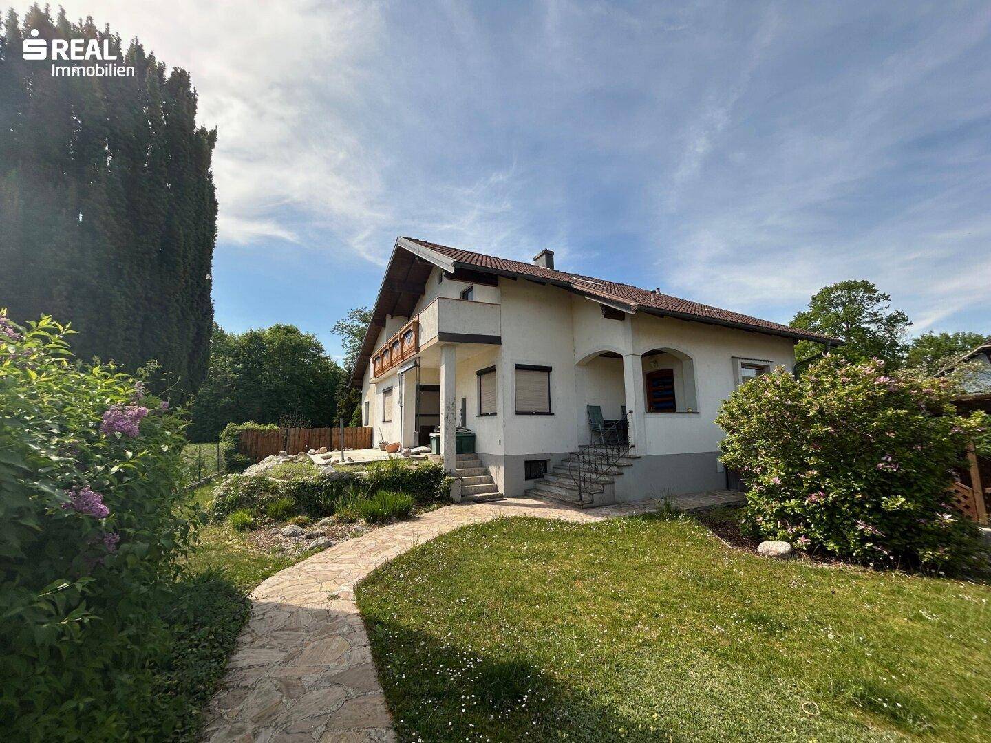 Charmantes Einfamilienhaus mit gepflegtem Vorgarten und Steinweg unter blauem Himmel.