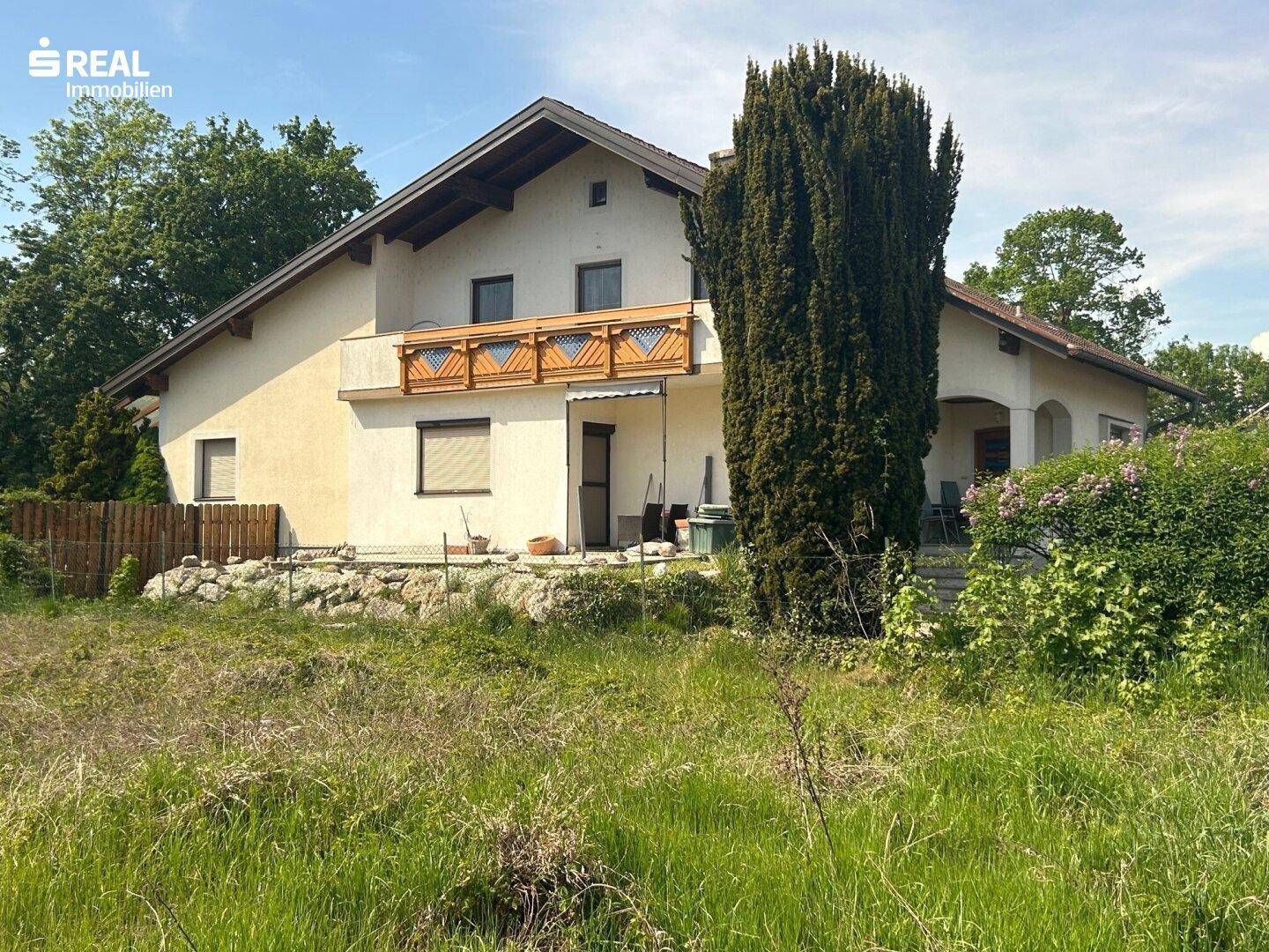 Seitenansicht des Hauses mit Balkon und üppiger Vegetation im Vordergrund.