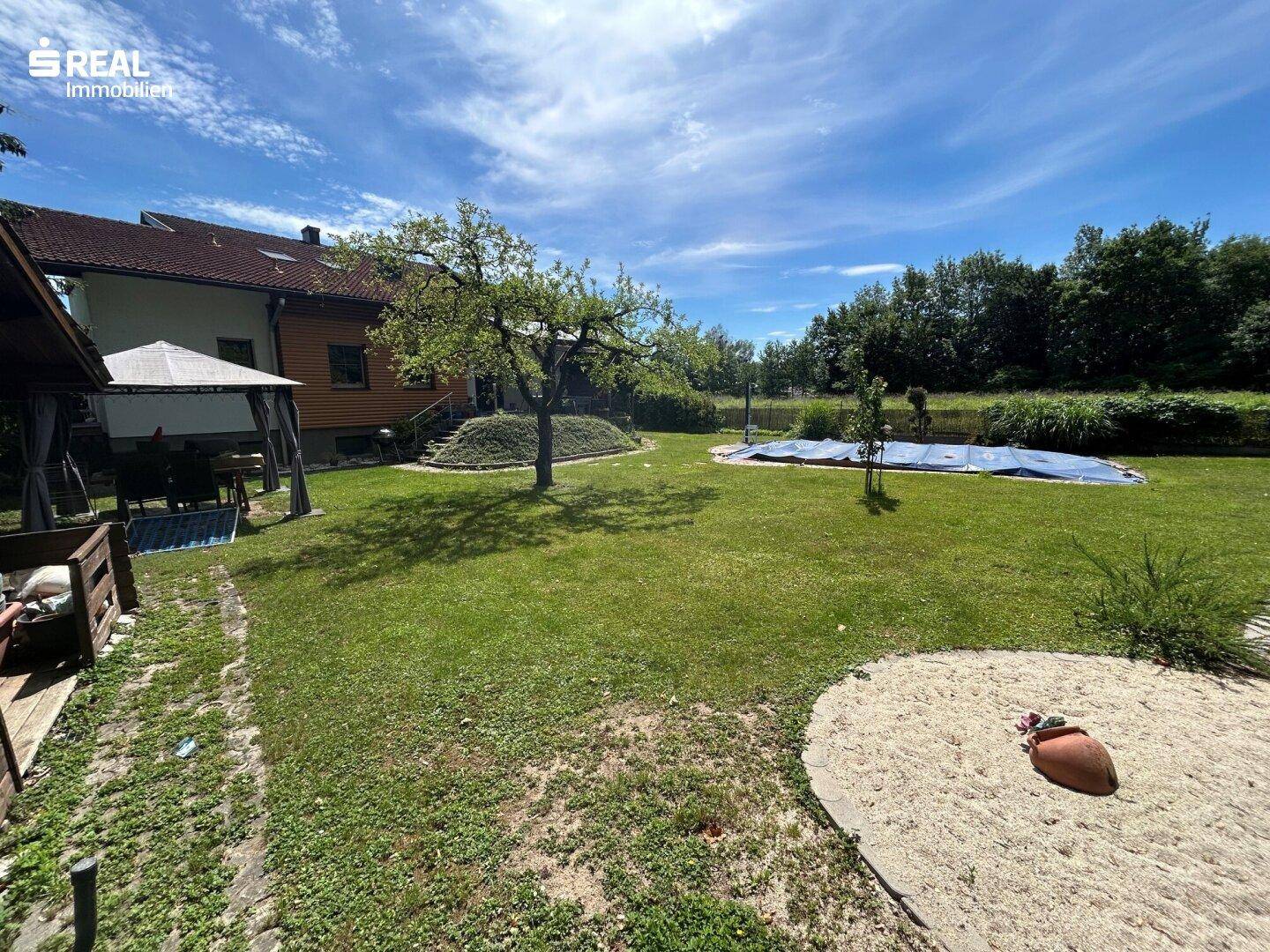 Großer, sonniger Garten mit Rasenfläche, Obstbaum und abgedecktem Poolbereich.
