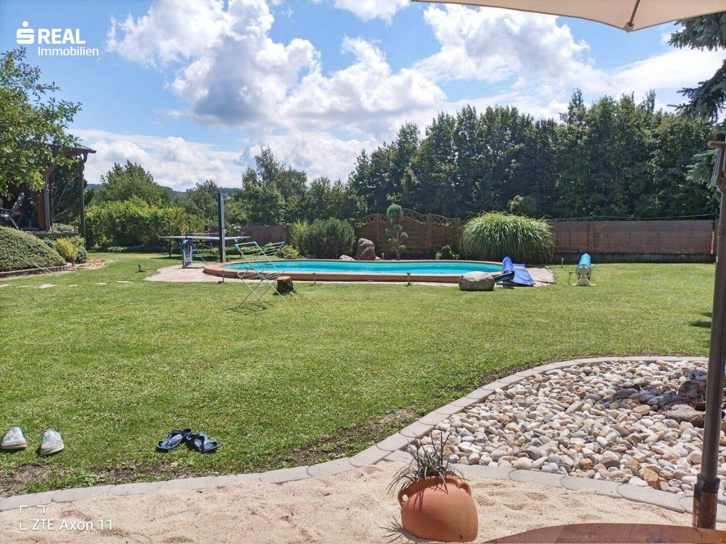 Sonniger Garten mit ovalem Pool, Sandbereich und Liegestühlen für Entspannung.