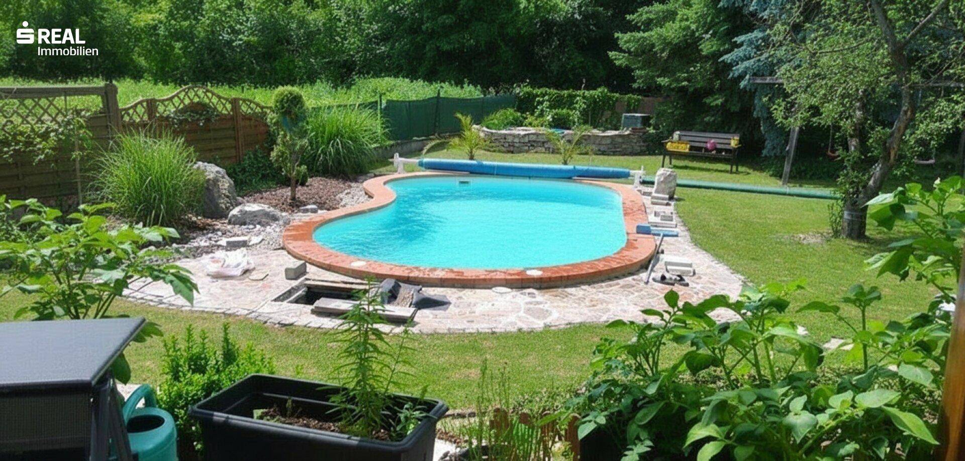 Herzförmiger Pool im Garten, umgeben von üppigem Grün und einer Holzumzäunung.