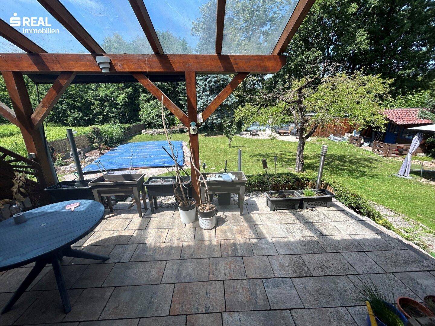 Überdachte Terrasse mit Fliesenboden und weitem Blick in den grünen Garten.