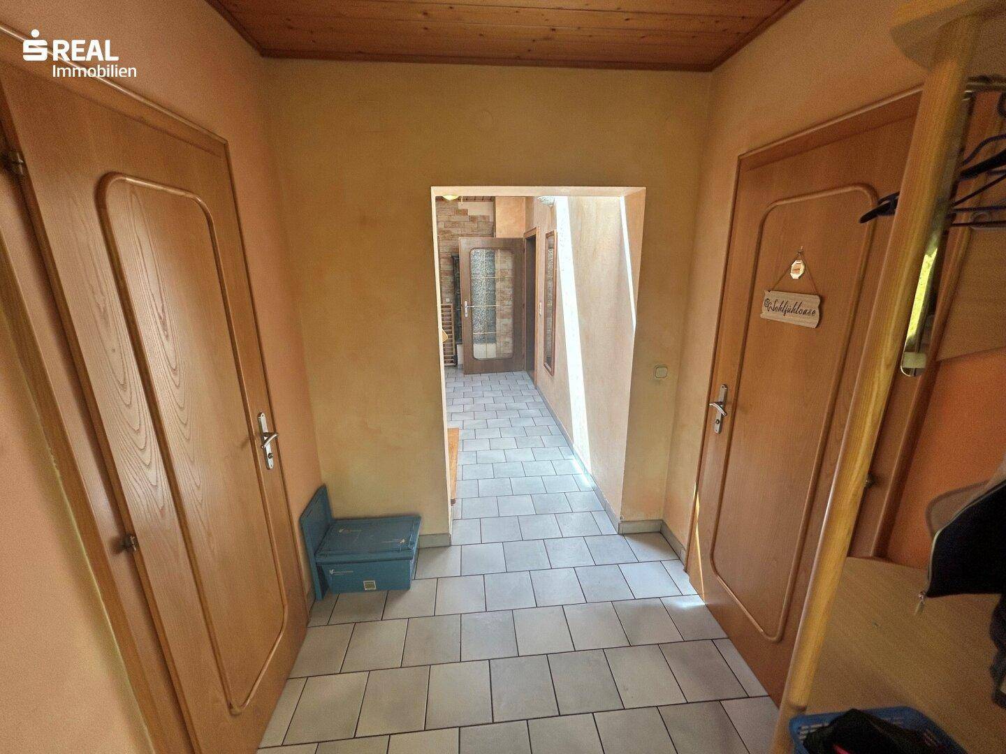 Heller Flur mit weißen Fliesen, Holzdecken und Zugang zu verschiedenen Räumen.
