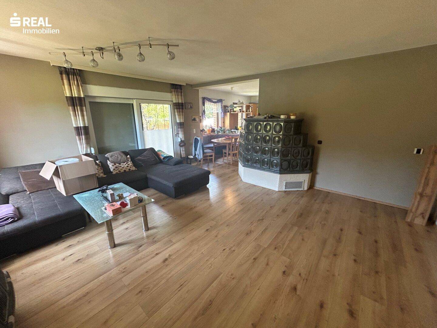 Geräumiges Wohnzimmer mit Laminatboden, Kachelofen und Zugang zur Terrasse.