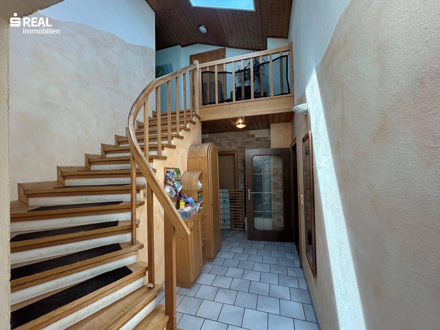 Geschwungene Holztreppe mit Fliesenboden im Eingangsbereich, führt in die obere Etage.