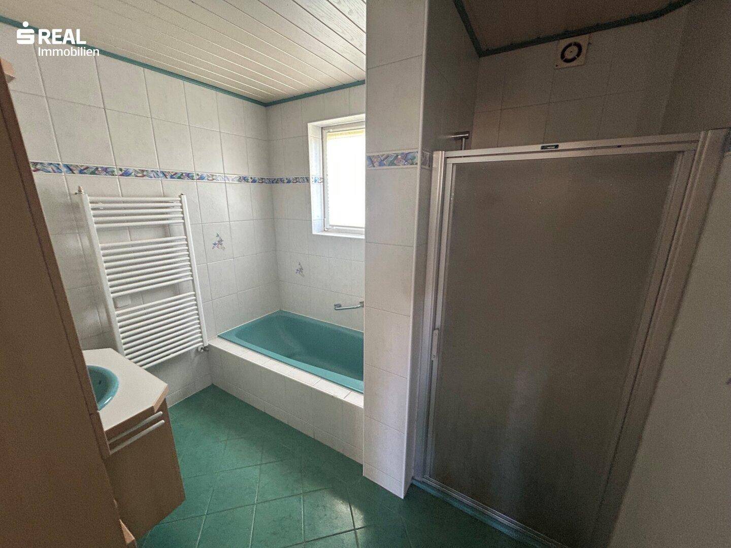 Älteres Badezimmer mit grünen Fliesen, Badewanne und Duschkabine.