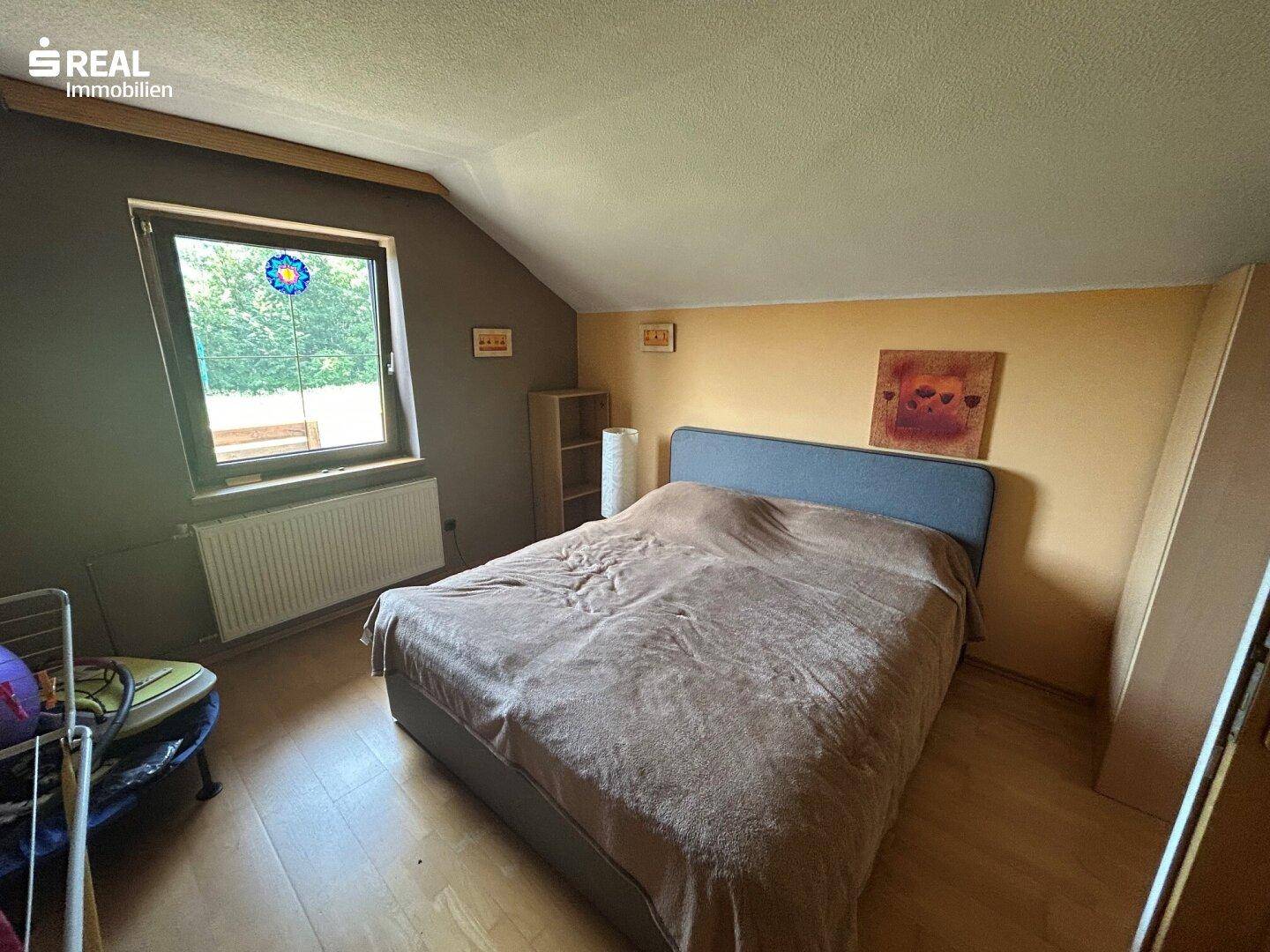 Schlafzimmer im Dachgeschoss mit schräger Decke, Laminatboden und Fenster.