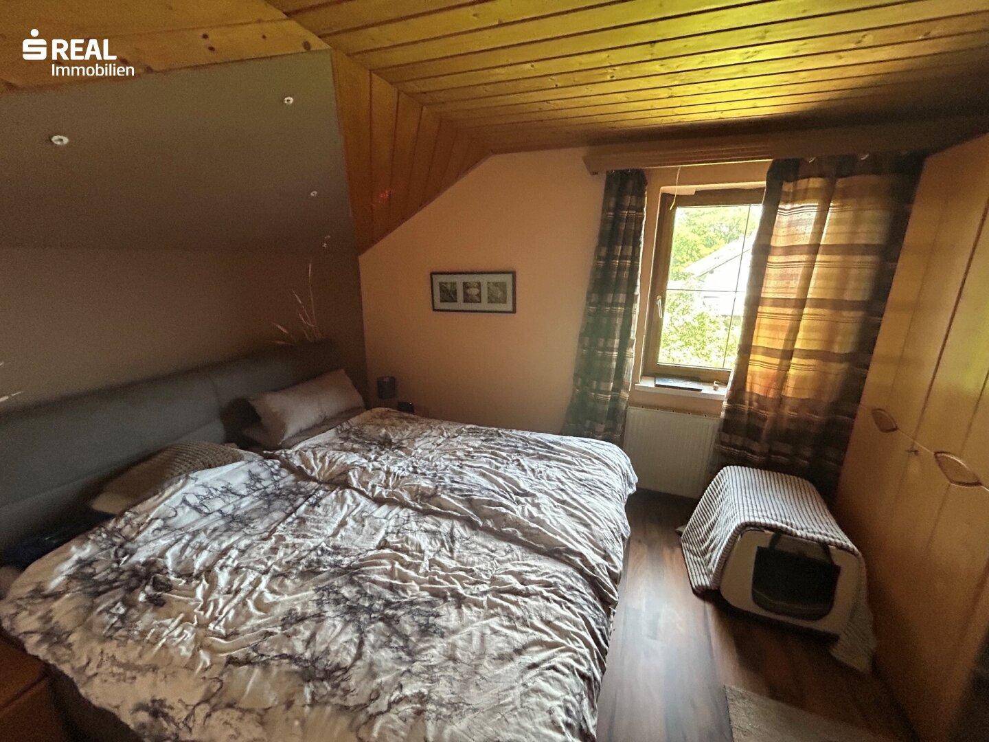 Gemütliches Schlafzimmer mit Holzdachschräge, Laminatboden und Fenster.