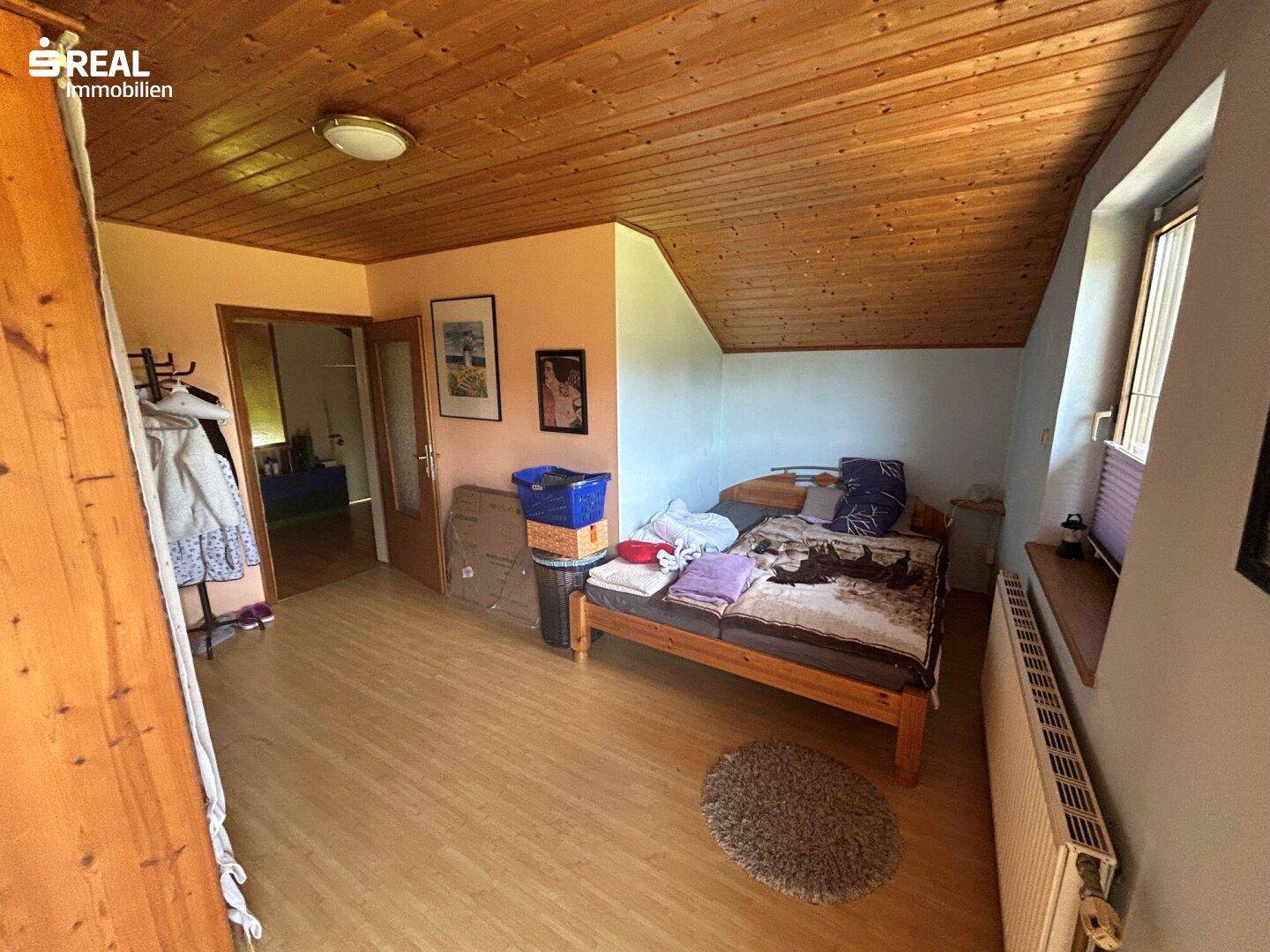 Helles Schlafzimmer im Dachgeschoss mit Holzdachschräge, Laminatboden und Kleiderschrank.
