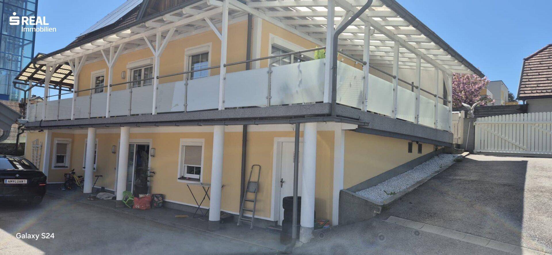 Ansicht des Gebäudes mit einem langen, überdachten Balkon und einer Zufahrt im Freien.