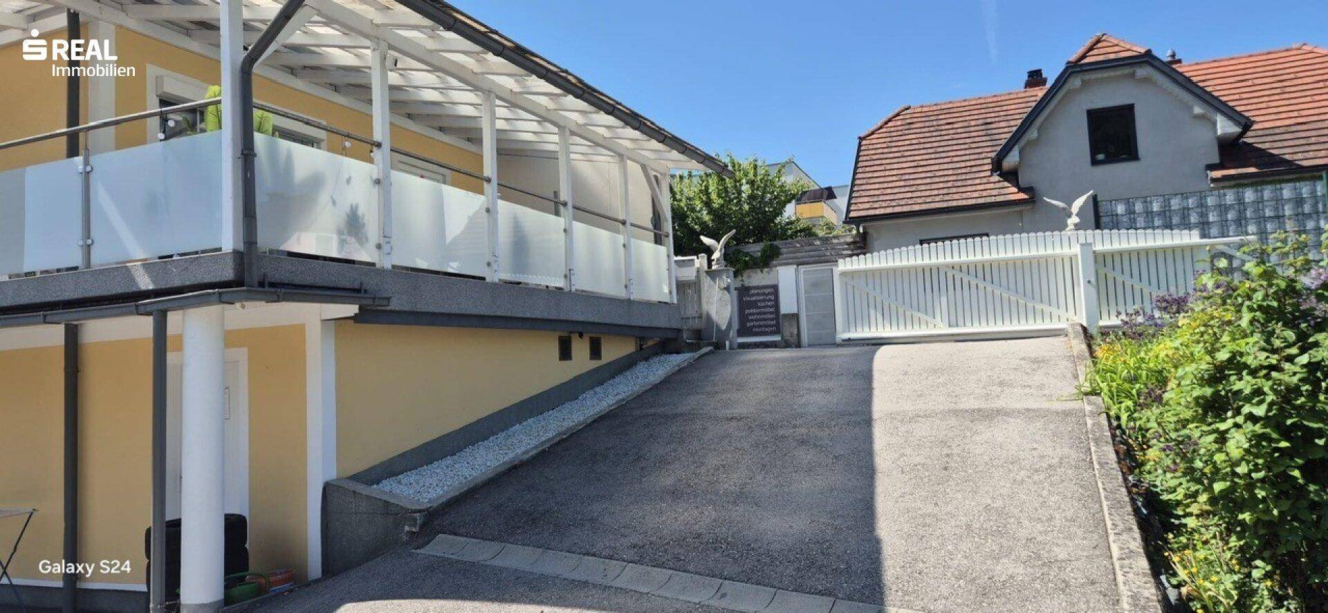 Zufahrt zum Grundstück mit angrenzendem Gebäude und einem weiteren Haus im Hintergrund.