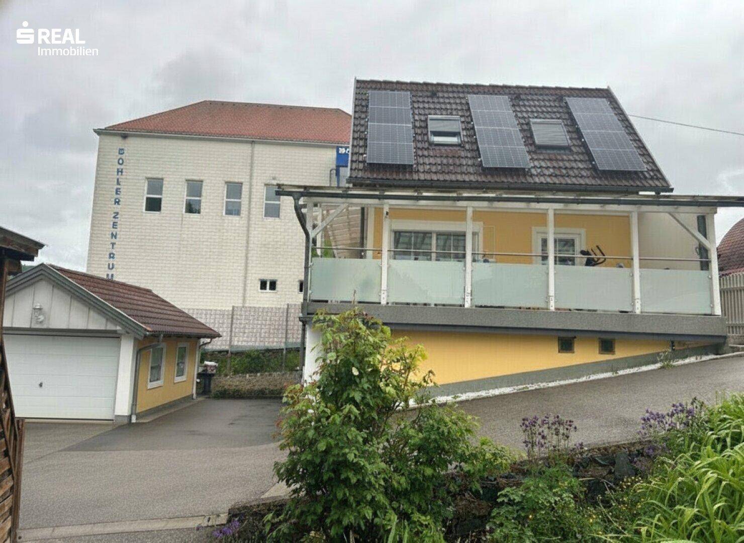 Gebäudeansicht mit Solarmodulen auf dem Dach und einer separaten Garage auf dem Grundstück.