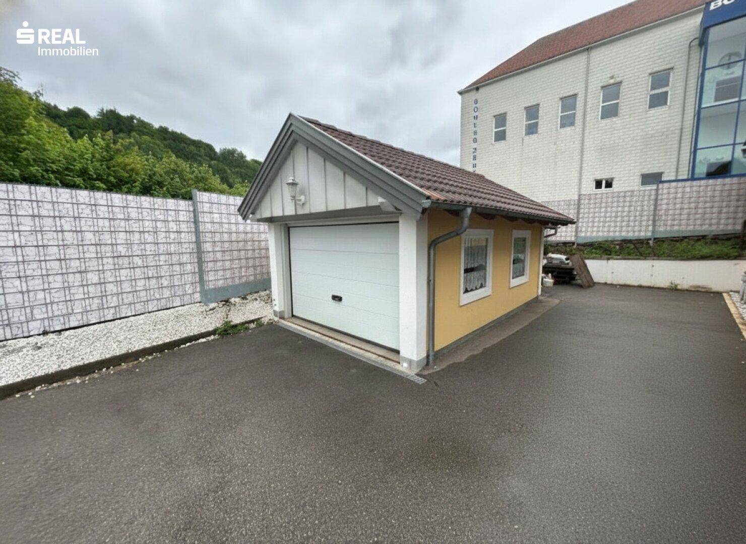 Separate Garage mit weißem Garagentor und kleineren Fenstern auf dem Grundstück.