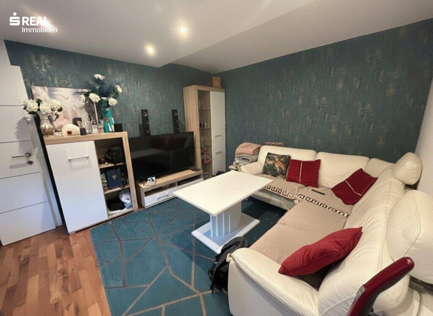 Wohnzimmer mit weißem Ecksofa, dunkler Tapete und Teppichboden in modernem Design.