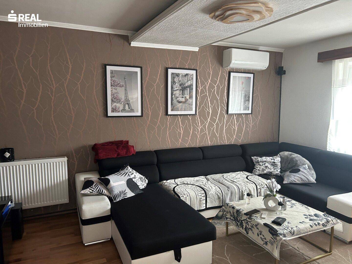 Gemütliches Wohnzimmer mit großem Ecksofa, gemusterter Tapete und Klimaanlage.