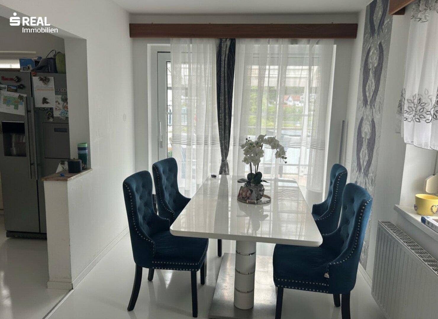 Heller Essbereich mit modernem Esstisch, blauen Samtstühlen und Zugang zum Balkon.