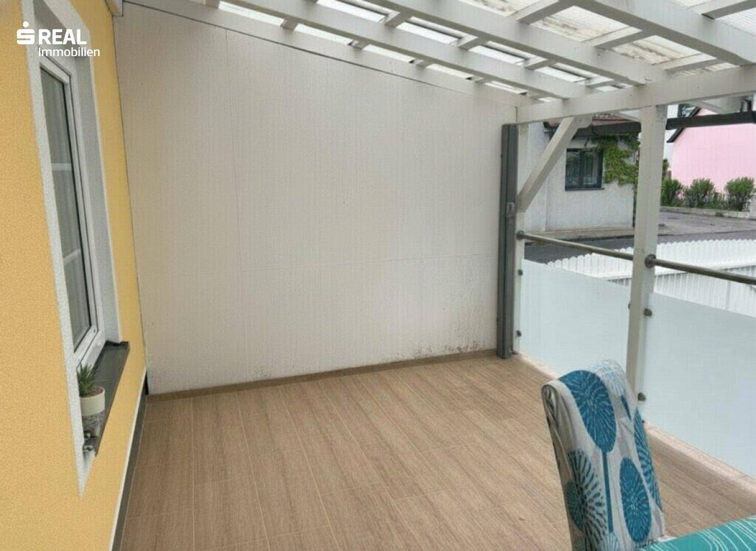 Teil des überdachten Balkons mit Holzbodenfliesen und einem Stuhl für den Außenbereich.