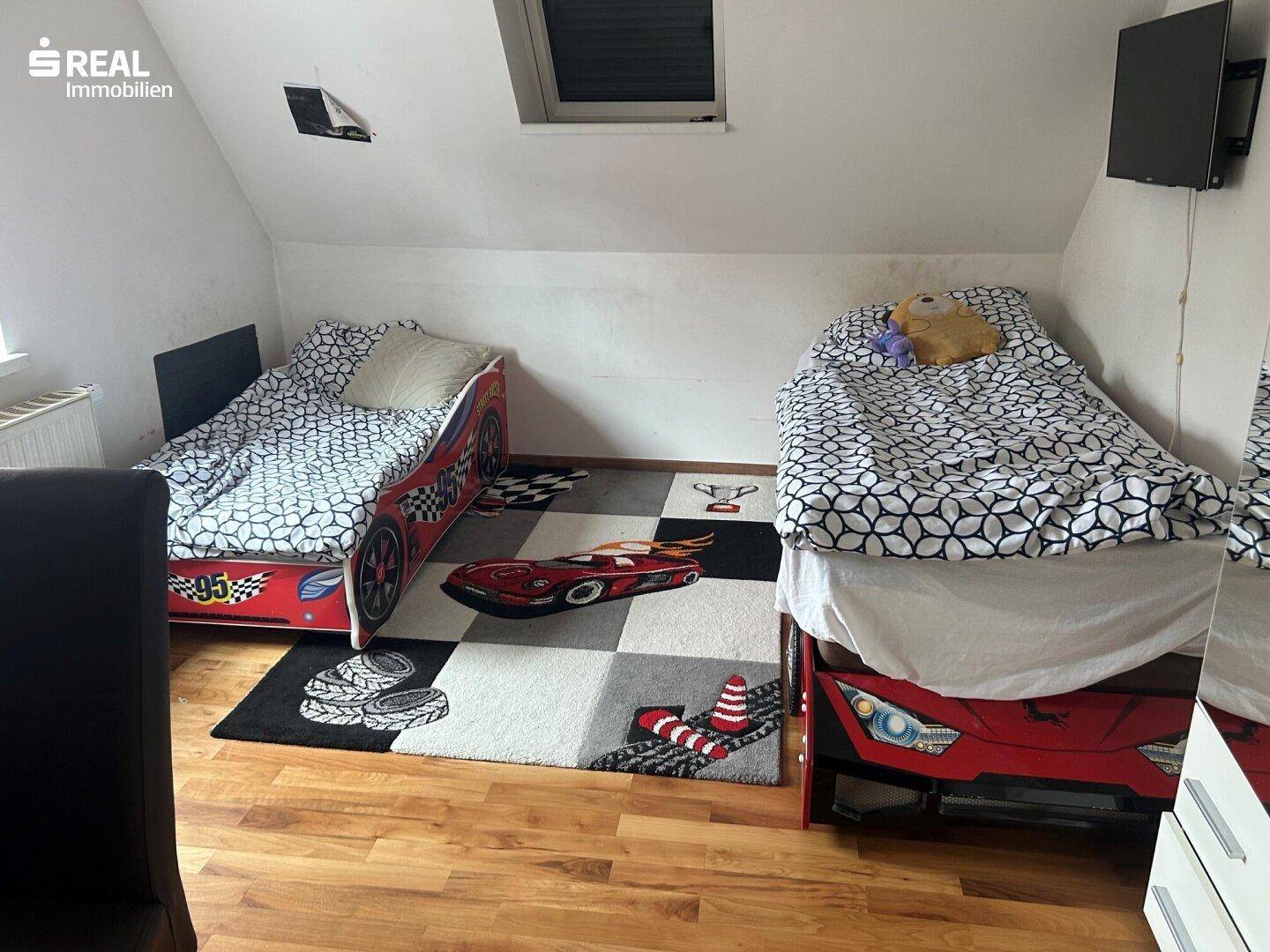 Kinderzimmer mit zwei Betten im Rennwagen-Design, Holzboden und Dachfenster.