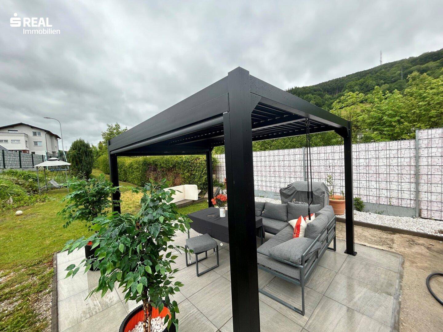 Gartenbereich mit moderner Pergola, Outdoor-Sitzgruppe und gepflasterter Terrasse.