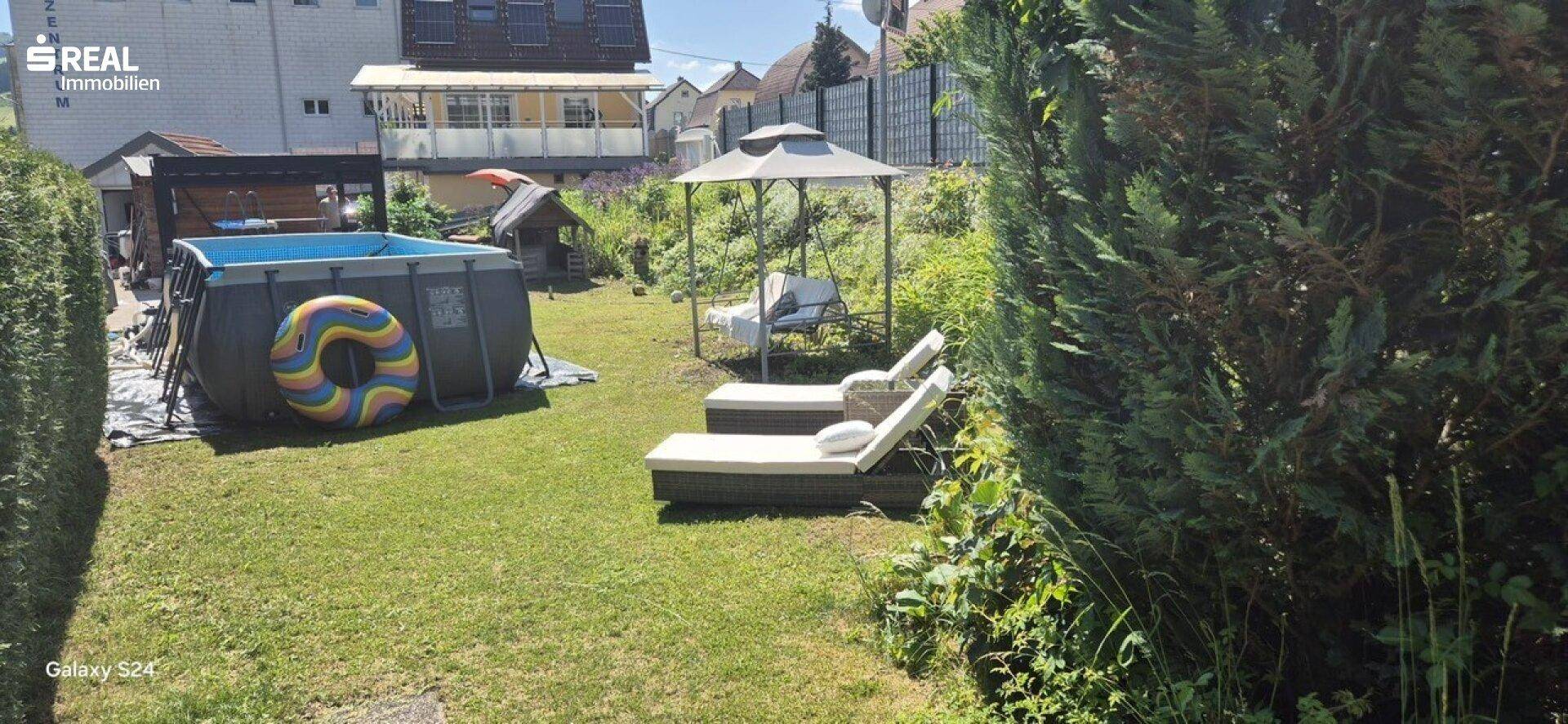 Sonnige Gartenfläche mit Rasen, Aufstellpool und Liegestühlen für Entspannung im Freien.