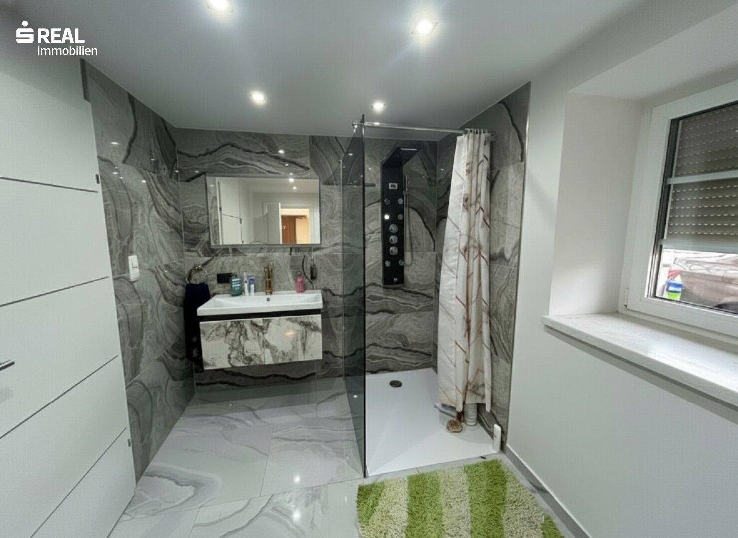 Modernes Badezimmer mit großformatigen Marmorfliesen, begehbarer Dusche und Fenster.